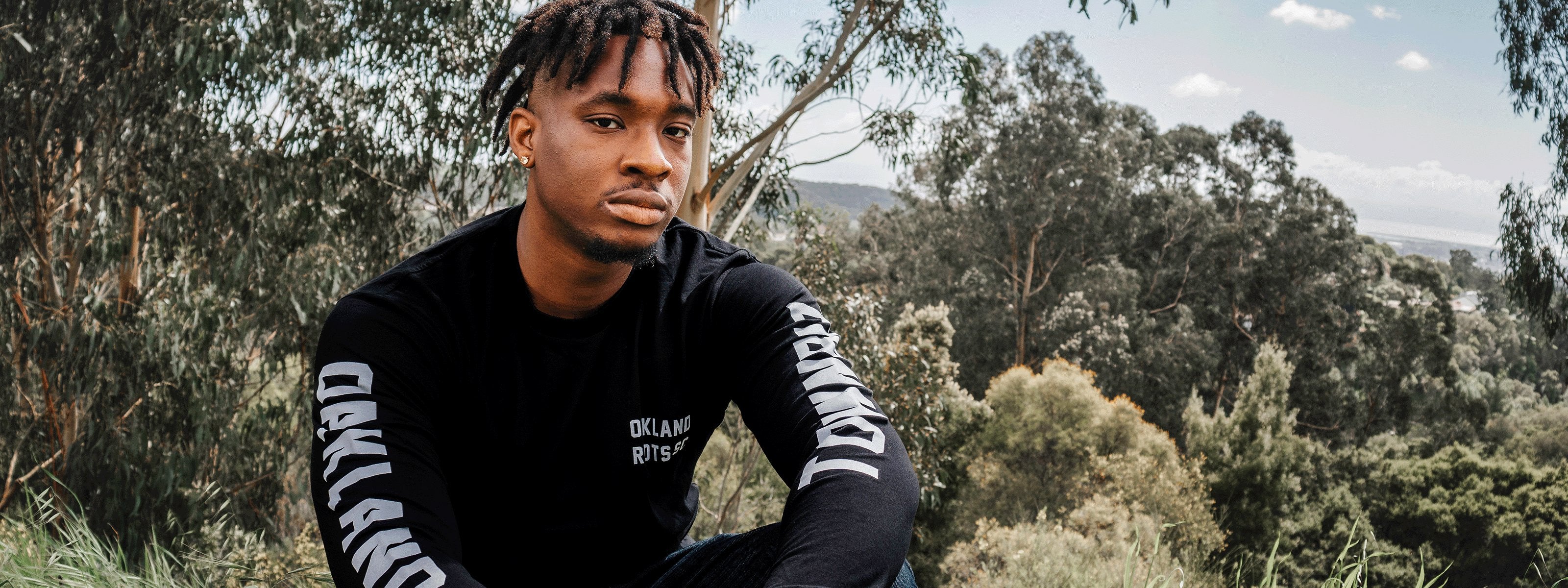 Man wearing a black tee with Oakland Roots Logo.