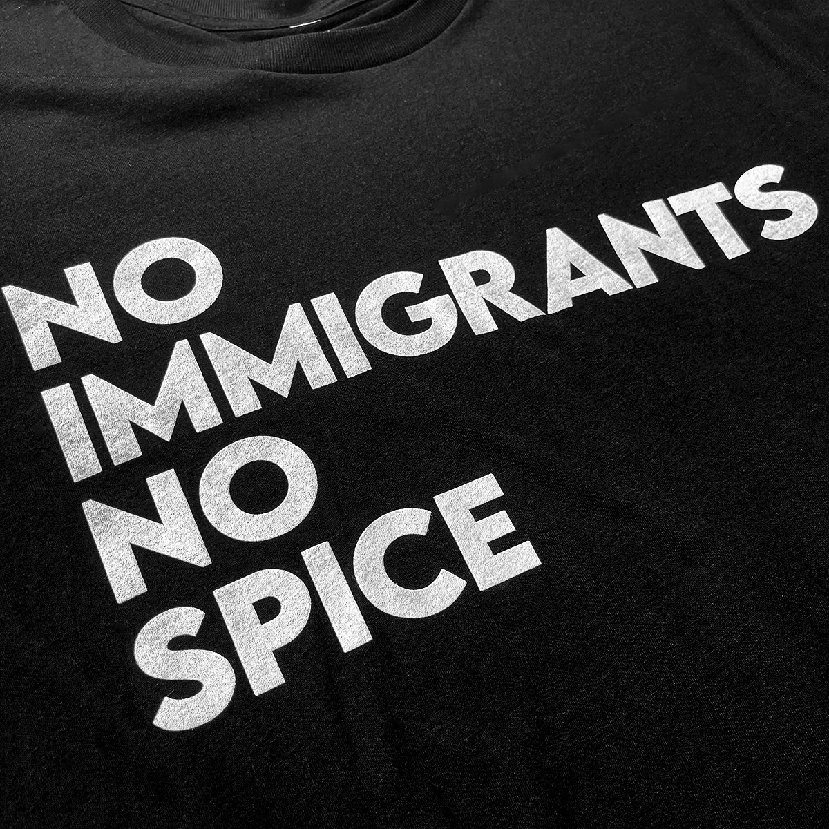 The NINS Classic Tee by Oaklandish features bold white text "NO IMMIGRANTS NO SPICE" on a black t-shirt. The perfectly aligned message, celebrating #spicypride, is clearly displayed for all supporters of immigrant rights.