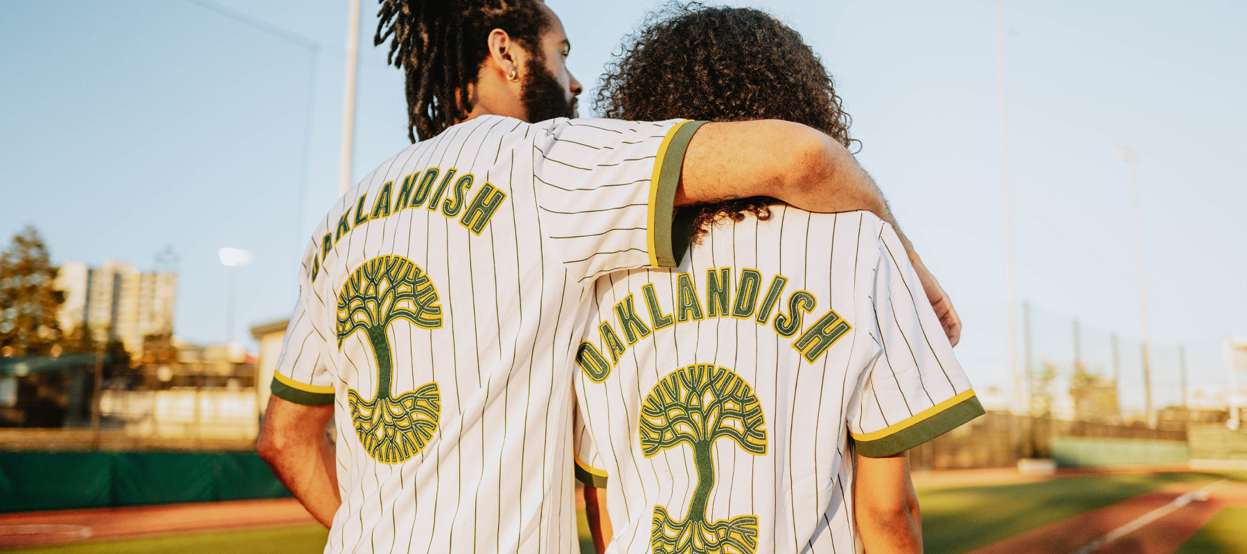 Man and Women on baseball field wearing white pinstripe jerseys with Oaklandish and Logo on back.