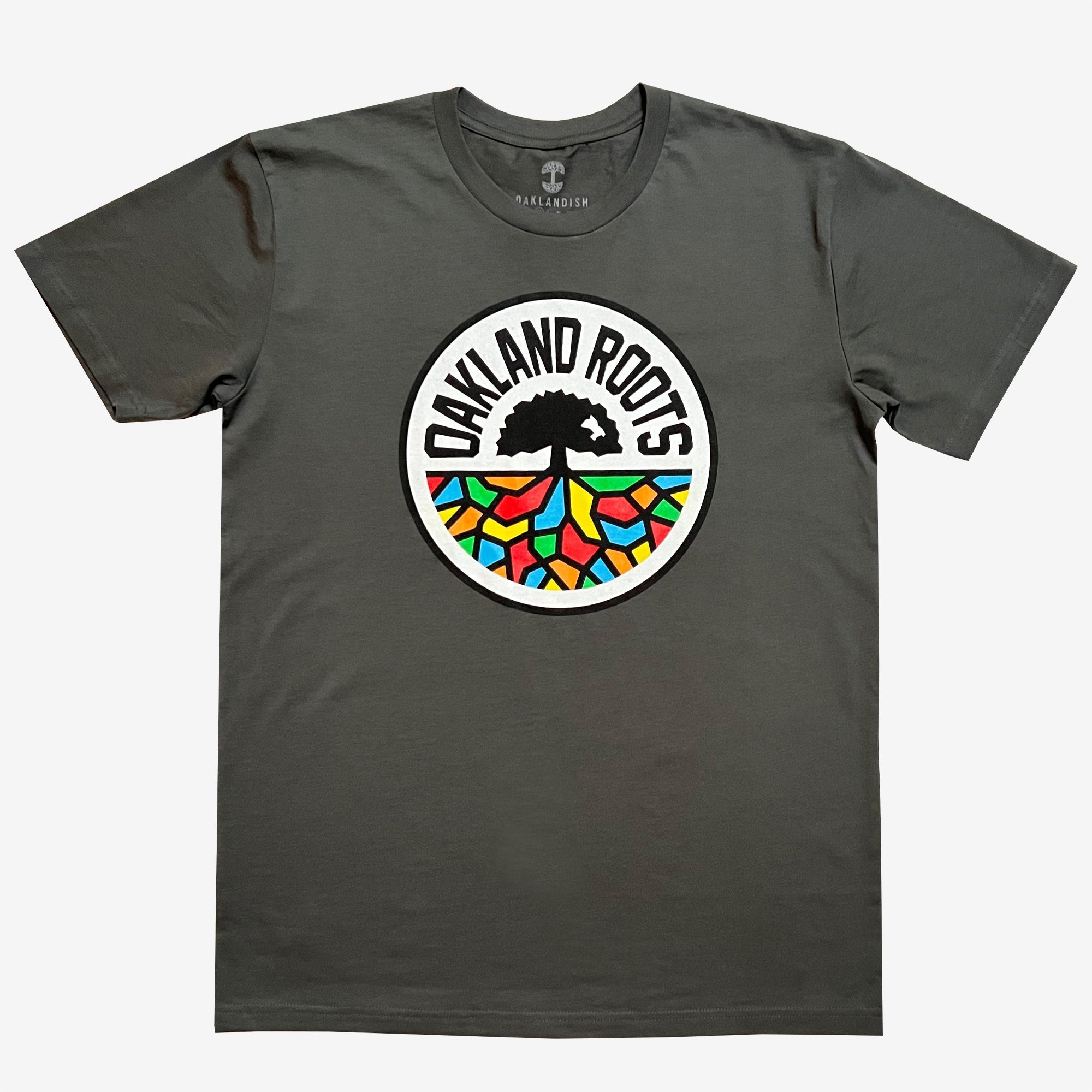 Introducing the Oakland Roots SC Classic Tee by Oakland Roots SC: a charcoal gray T-shirt prominently featuring the "Oakland Roots" logo at its center. The logo, inspired by the Oaklandish aesthetic, showcases a tree with extensive roots forming vibrant mosaic-like patterns in shades of red, blue, green, yellow, and orange. The text "OAKLAND ROOTS" elegantly arches over the tree and its colorful roots.