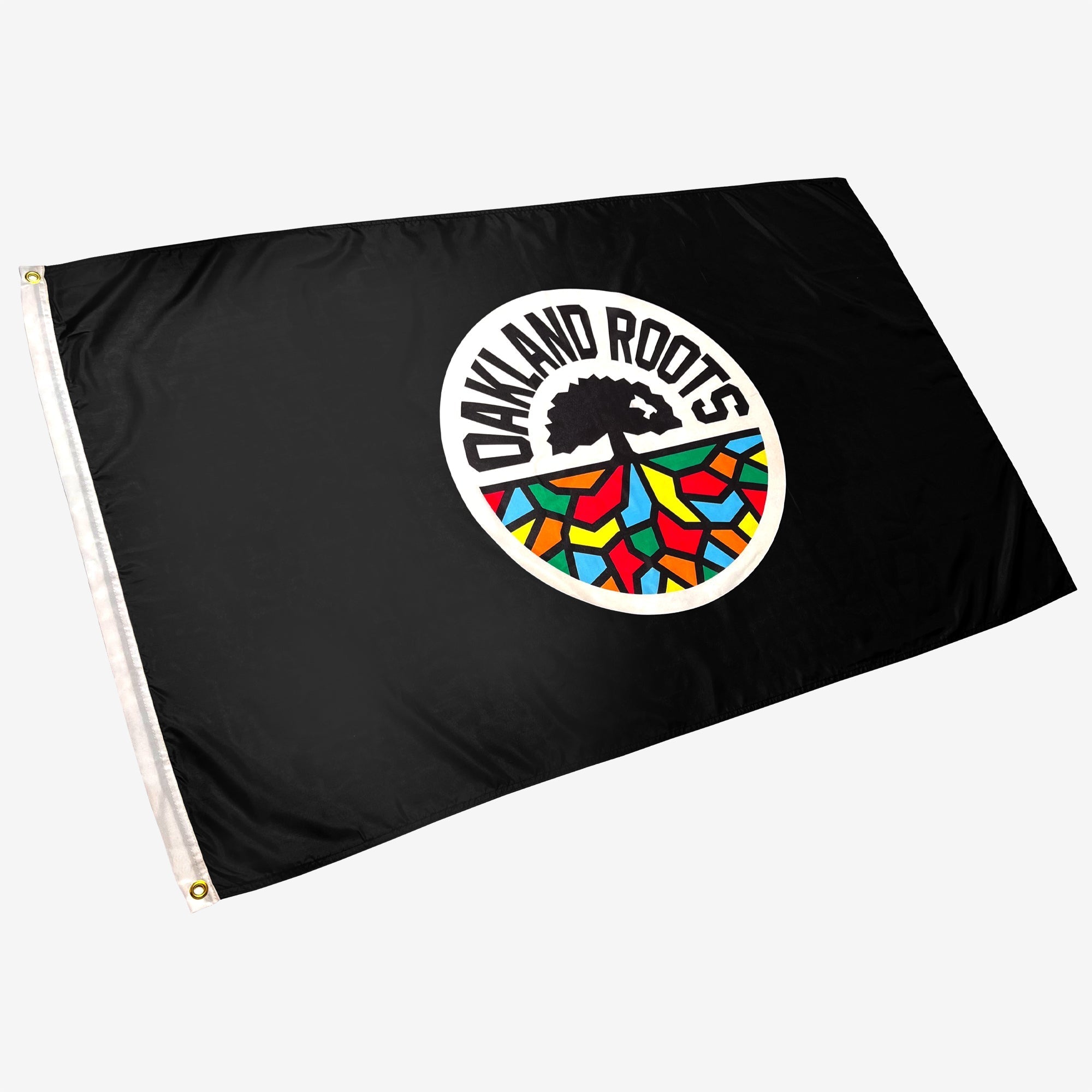 The Oakland Roots SC Logo Flag is a black flag showcasing the Oakland Roots Sports Club logo in the center. The circular logo features a tree with exposed roots, encircled by vibrant geometric patterns in red, blue, yellow, and green. The words "OAKLAND ROOTS" curve above the tree.