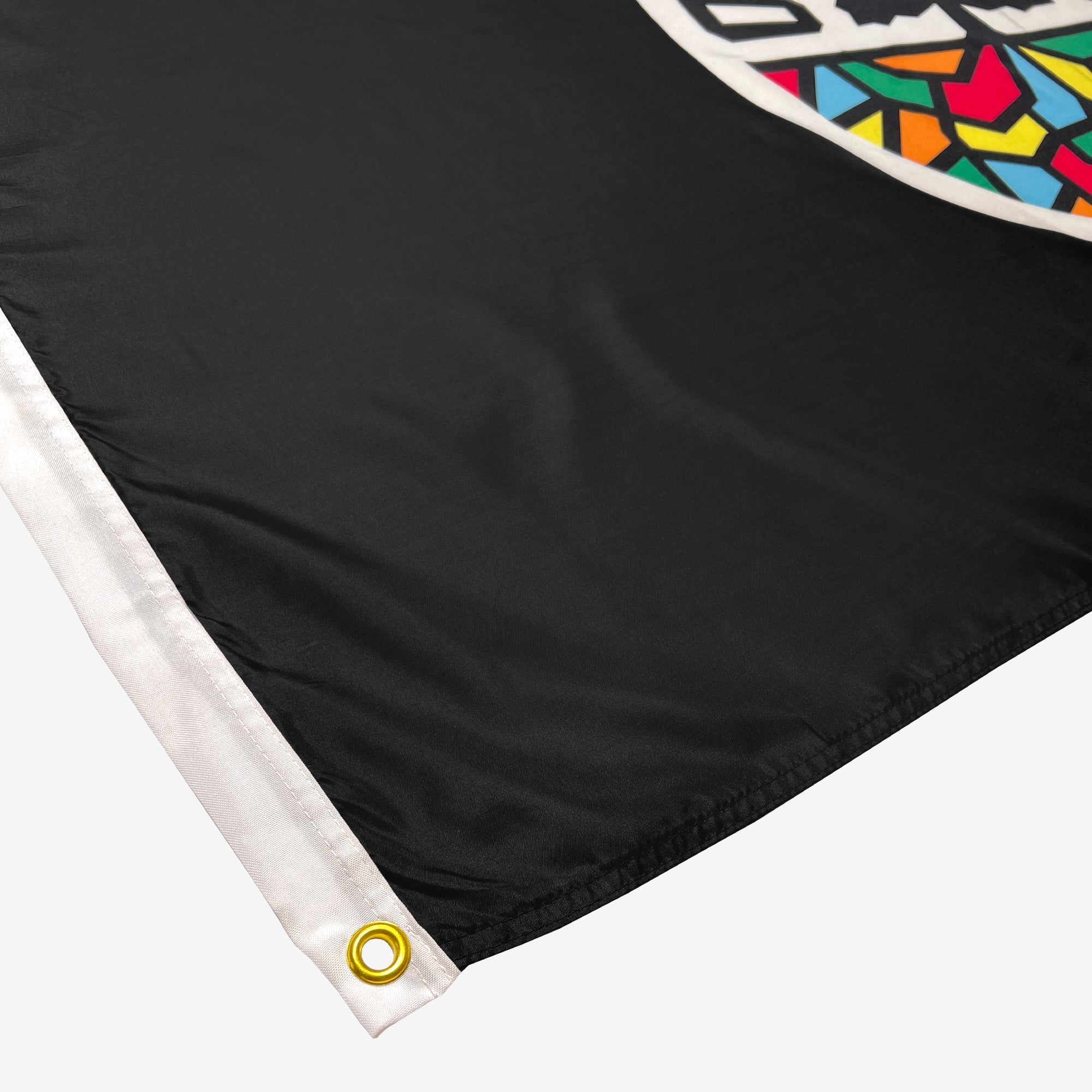 Close-up image of the Oakland Roots SC Logo Flag by Oakland Roots SC, featuring two metal grommets on a black flag with white trim on the hoist; one grommet is visible in gold color. The flag showcases a vibrant, colorful geometric pattern in the upper right corner, reminiscent of the dynamic energy of Oakland Roots Sports Club.