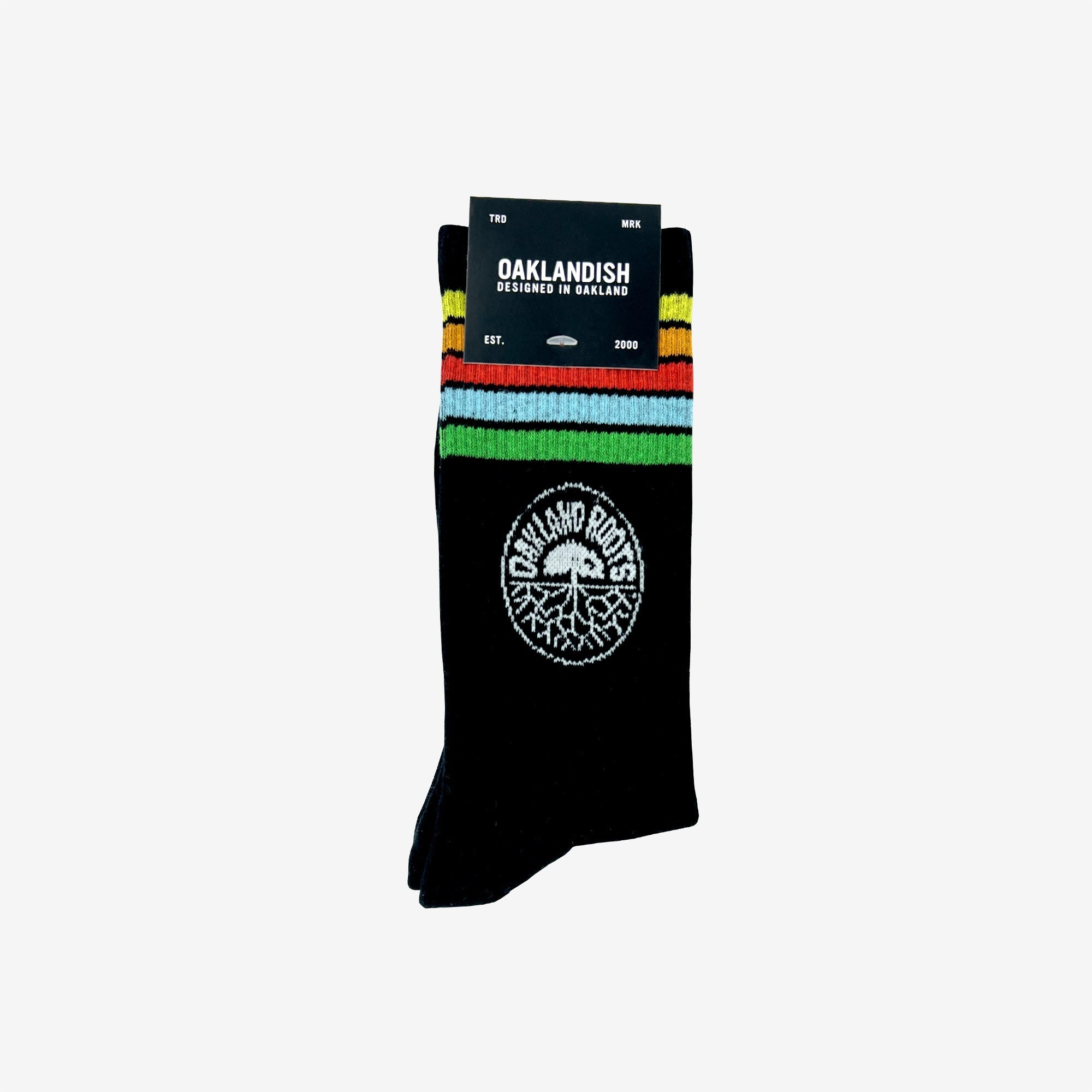 The Oakland Roots SC Stripes Sock is a pair of black crew socks adorned with vibrant red, yellow, and green stripes near the top. These socks display a white circular Oakland Roots logo featuring a tree and "OAKLAND ROOTS" text on the lower part. A black label reading "OAKLANDISH" along with additional product details is attached to the socks.