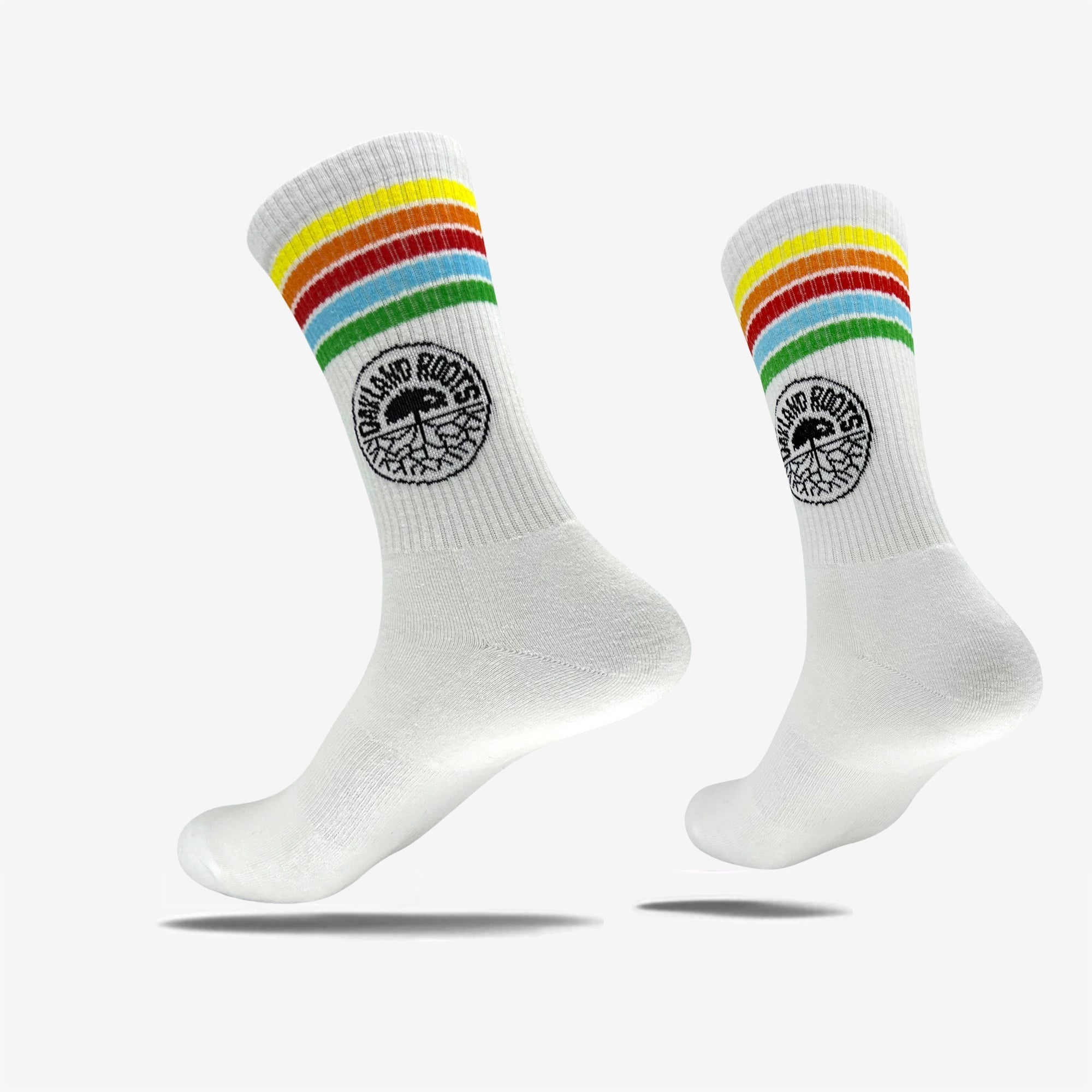 The Oakland Roots SC Stripes Sock is a pair of white crew socks with vibrant yellow, red, and green stripes at the top. Adorned with a black round logo featuring the text "SIXLAND ROOTS" and an image of a tree, these socks are perfect for any Oakland Roots Sports Club fan. They are displayed in an elevated position with shadows cast beneath them.