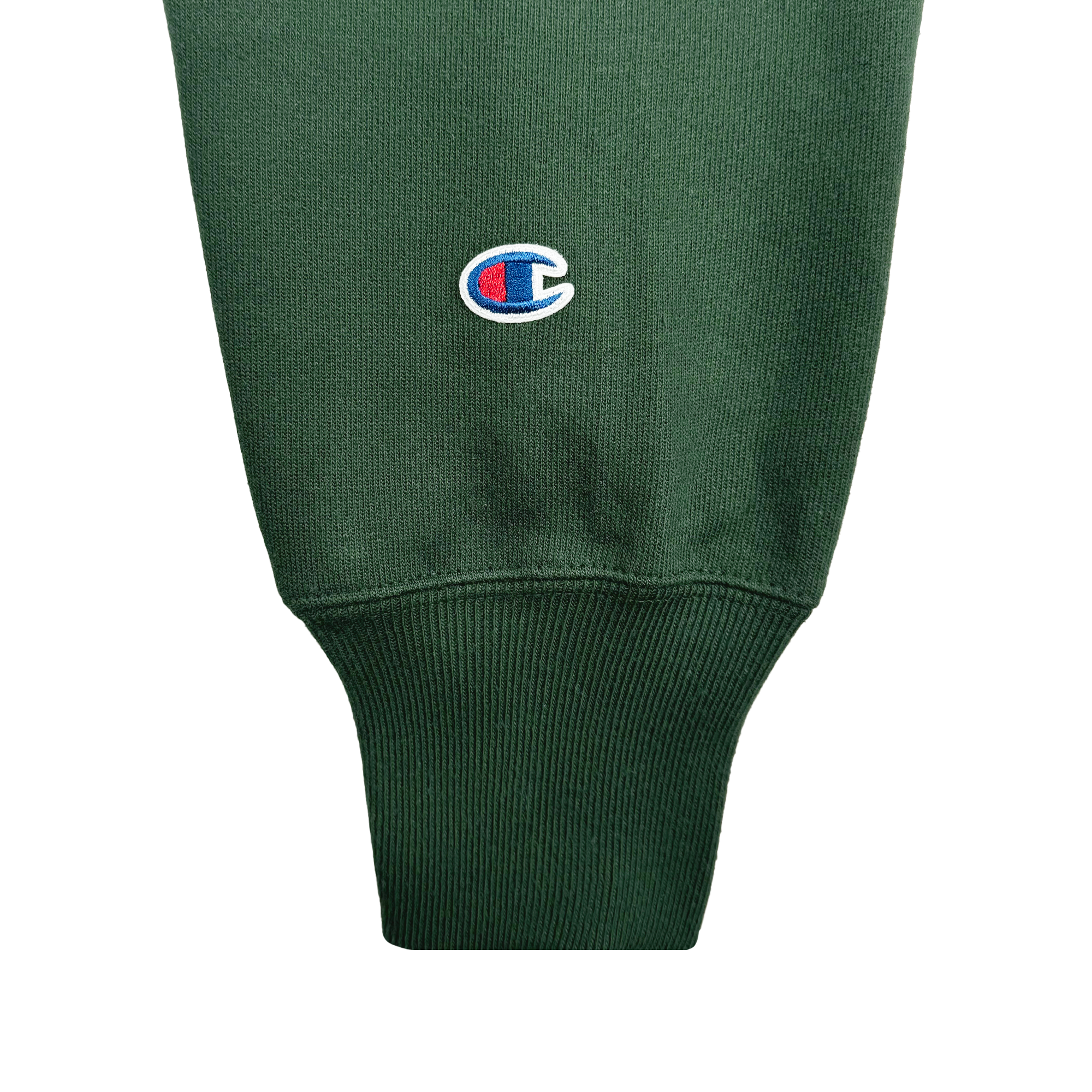 Close-up of a green sleeve from the Champion X Oakland Ballers Logo Hoodie, featuring a ribbed cuff. The textured fabric displays an embroidered multicolored "C" logo, stitched in blue, red, and white. The lighting highlights the material's weave and the logo's vibrant colors, capturing the dynamic spirit of the Oakland Ballers.