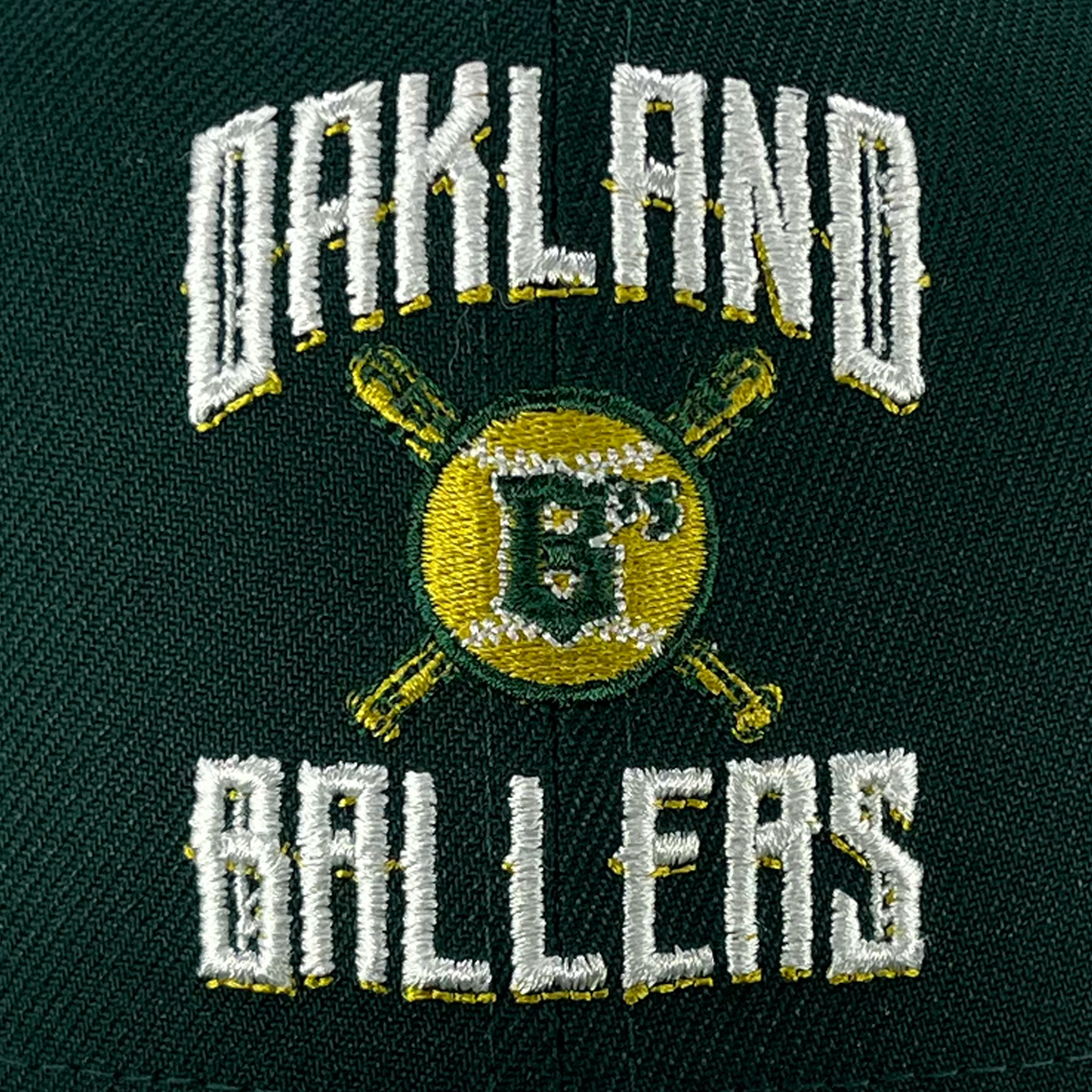 Close-up of the New Era Oakland Ballers Alt. Logo 59FIFTY Cap displaying the embroidered logo of the Oakland Ballers, a team in the Pioneer League. The logo features a yellow baseball with two crossed green bats behind it and the initials "OB" overlaid. "Oakland" above and "Ballers" below are stitched in bold white letters, reminiscent of Oaklandish logos.