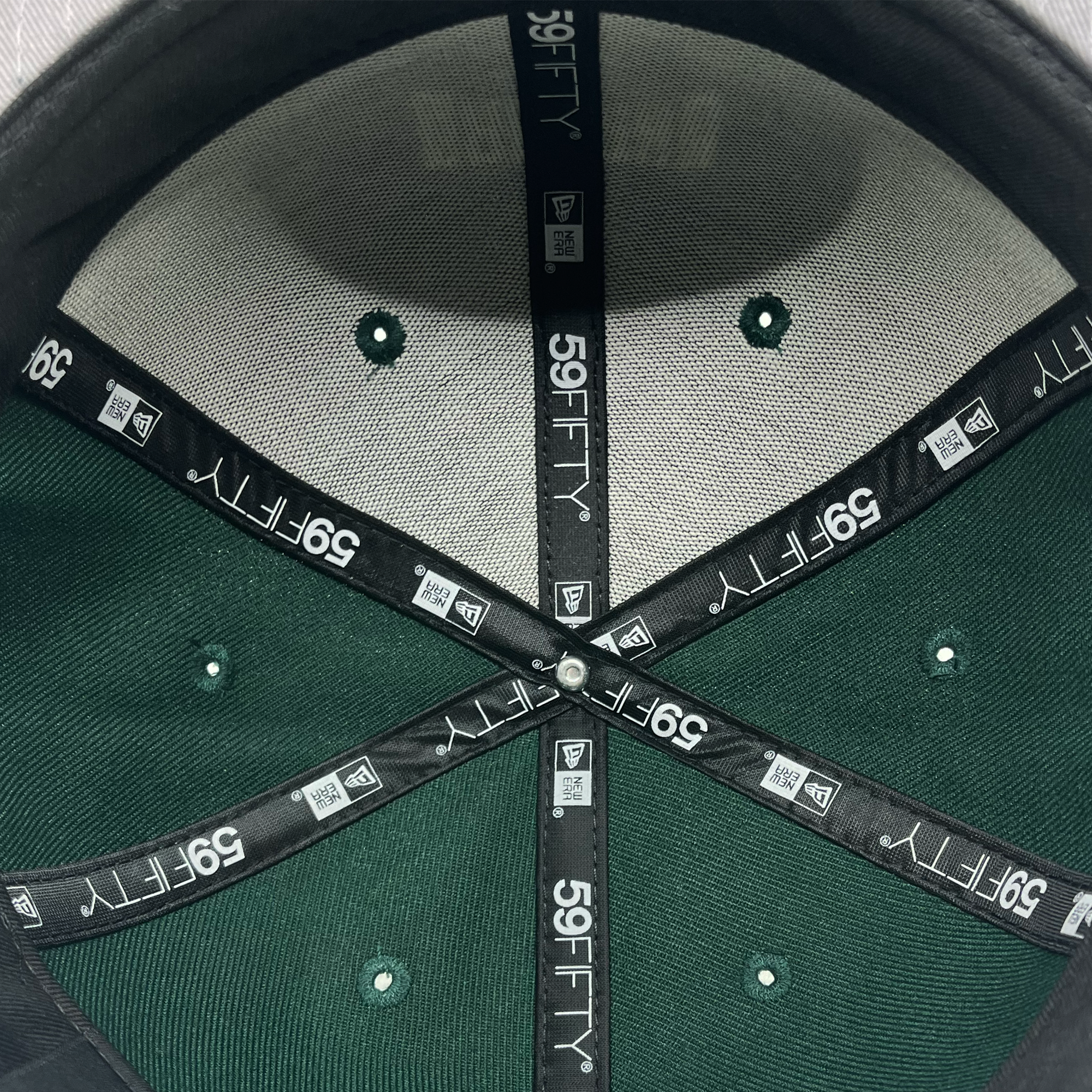 The image illustrates the interior of a New Era Oakland Ballers Alt. Logo 59FIFTY Cap. The hat has a black inner band adorned with white "59FIFTY" branding that spans from the center of the dome to its edges. Reflecting the Oakland Ballers' colors, the interior comprises grey and green hues, featuring six green rivets where each section intersects for ventilation.