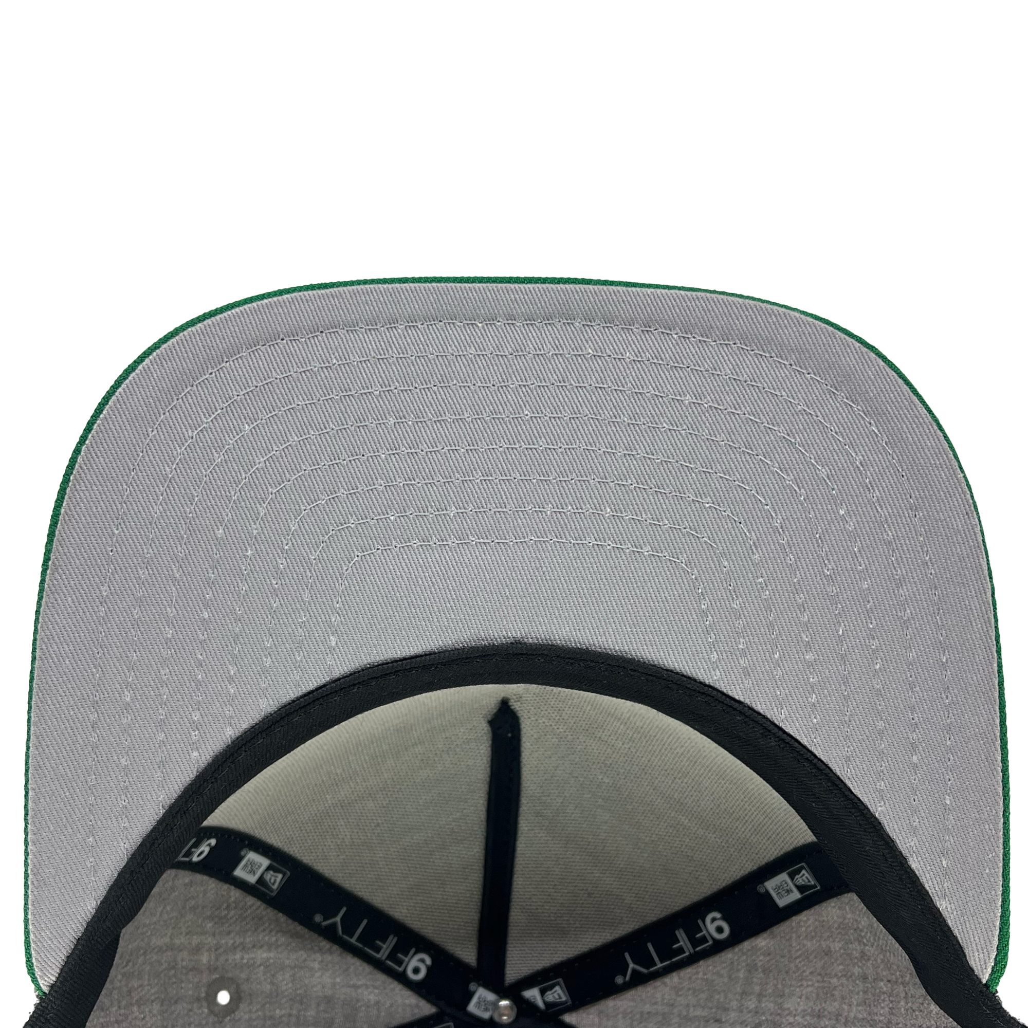 The image showcases the underside of the New Era Oakland Ballers Alt Logo 9FIFTY AF Cap. The stitching pattern on the grey fabric of the brim is prominently highlighted, with a green edge outlining it. Inside, black bands featuring "9FIFTY" and "Oakland Ballers" text are visible, indicating Oakland's new pro baseball team. The interior fabric is grey.