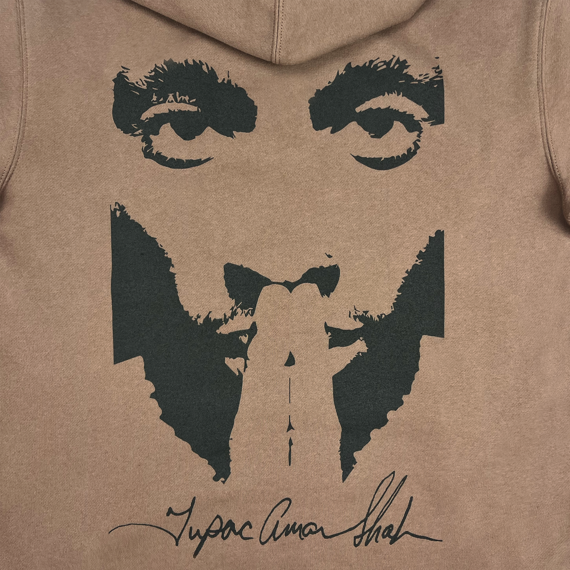 The Bless Hoodie by Oaklandish showcases a stylized portrait on a brown hoodie, featuring a person with fingers pressed together in front of their face. The design, rendered in black ink, highlights intense eyes and a serious expression. At the bottom is the signature "Tupac Amaru Shakur," marking this piece as an authentic collaboration between Oaklandish and Tupac.