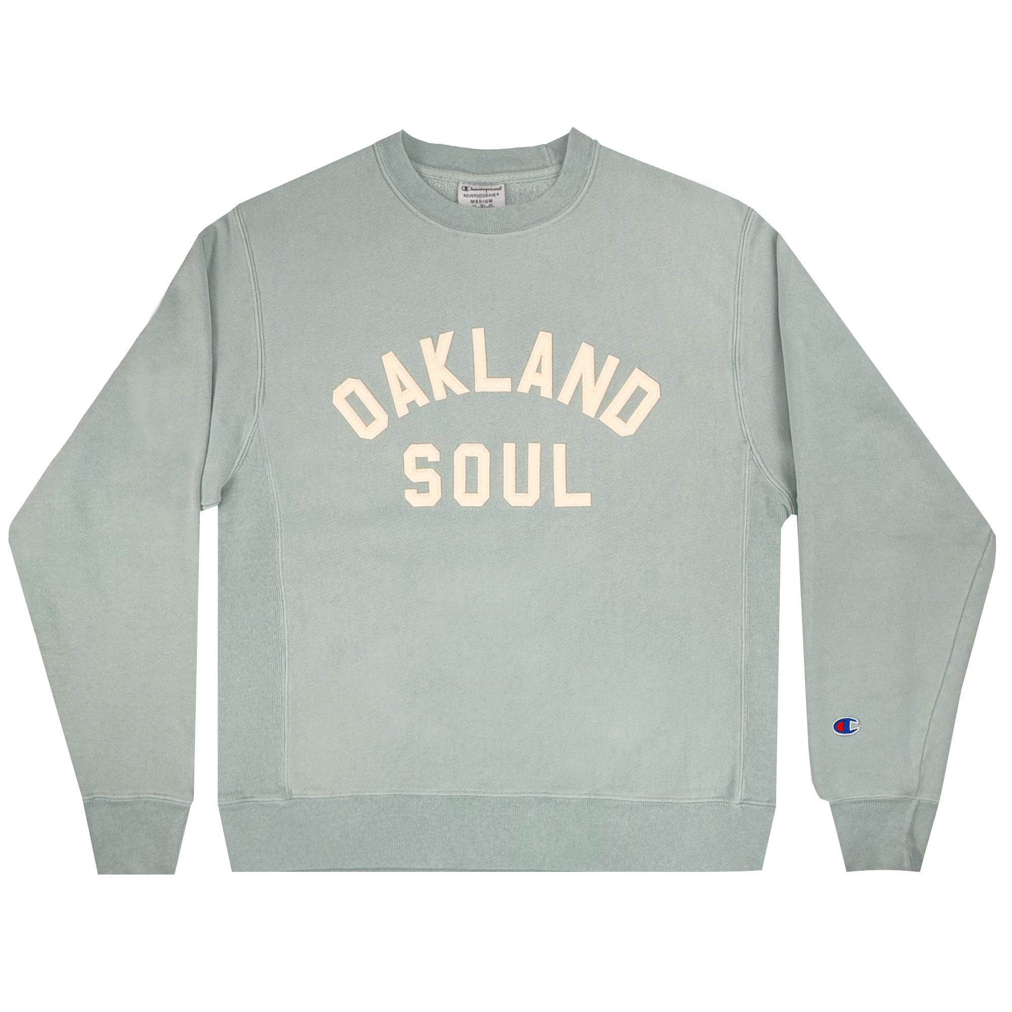 The Champion X Oakland Soul Wordmark Crew is a light green sweatshirt featuring "OAKLAND SOUL" in large white letters across the chest. It celebrates women's soccer, with long sleeves, ribbed cuffs and hem, and a small embroidered logo on the left sleeve near the cuff for a simple, casual look.