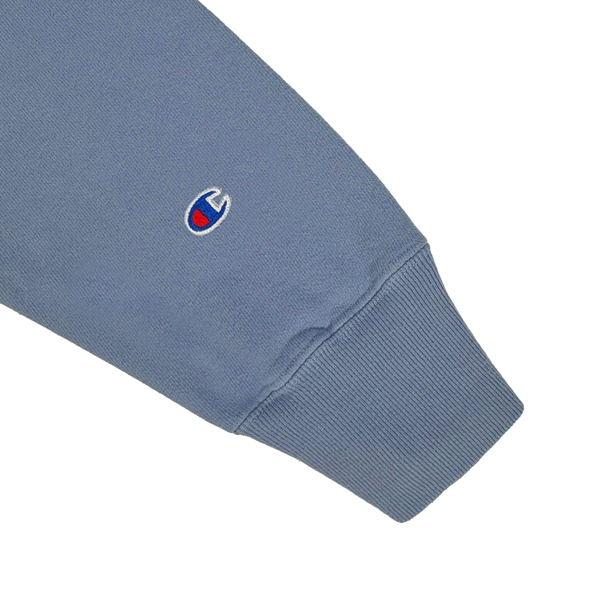 Close-up of the Champion X Oakland Soul Wordmark Crew sleeve: blue sweatshirt with a ribbed cuff, textured fabric, and a small blue and red embroidered logo capturing the vibrant energy of women's soccer teams like Oakland Soul.