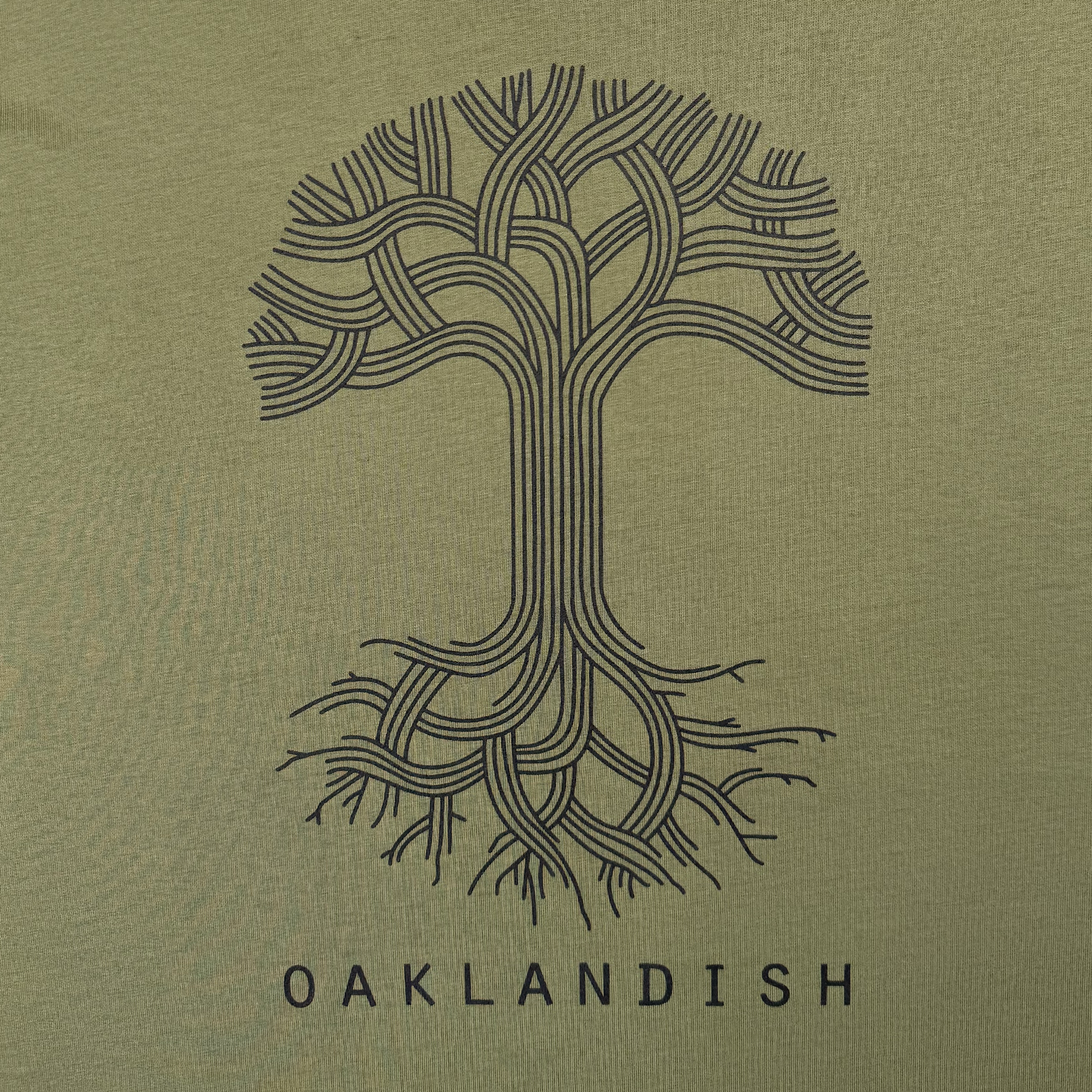 The Oaklandish Classic Logo Tee features a stylized black illustration of a T-shaped tree with intertwined branches and roots on a green background. "OAKLANDISH" is centered below in capital letters, capturing the brand's iconic design popular on their tees.