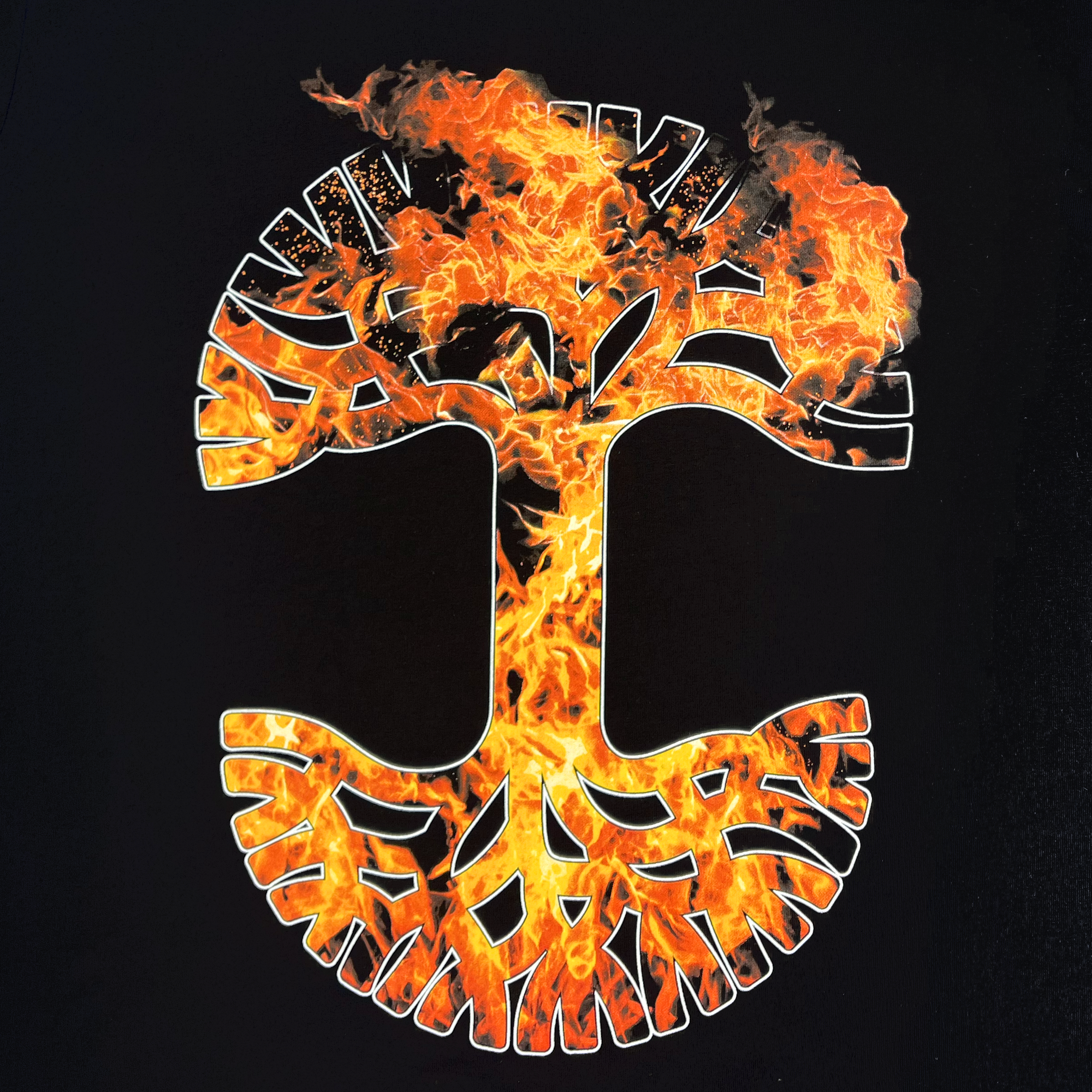 This striking art features a stylized tree design on a black background, with branches and roots depicted in white and partially filled with realistic, vivid flames of orange, yellow, and red. The flames spread out, giving the impression that the tree is burning. This captivating design is showcased on the Fuel Tee from Oaklandish's men's collection in a classic fit t-shirt.