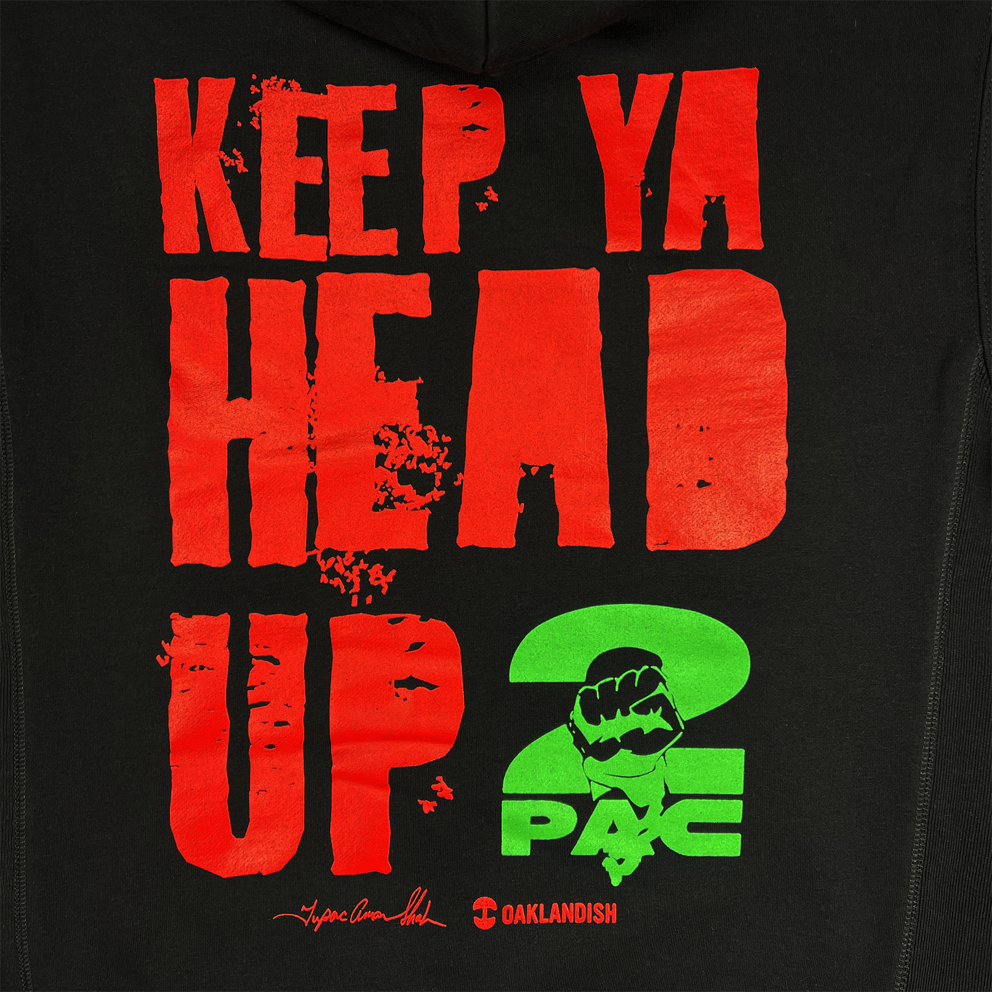 The black hoodie, featuring bold red text saying "KEEP YA HEAD UP" with a distressed look, showcases vibrant green "2 PAC" lettering next to a raised fist emblem. Celebrate Oakland culture with the Oaklandish x Tupac collaboration signature and logo on the lower section of the You Got To KYHU Hoodie by Oaklandish.