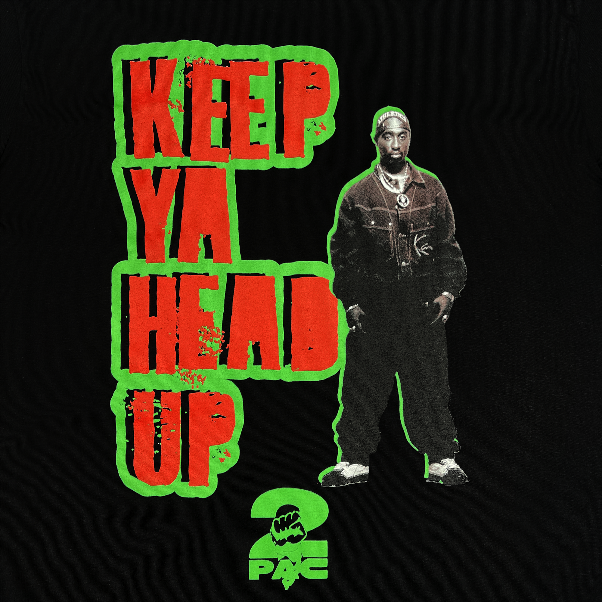 The "You Got To KYHU LS Tee" by Oaklandish features a graphic of a man wearing a jacket and pants beside the text "KEEP YA HEAD UP" in bold red block letters outlined in green. Beneath this, there's a small green fist and the name "2 PAC" in bold lettering. This collaboration honors Tupac's cultural influence on Oakland against a black background.