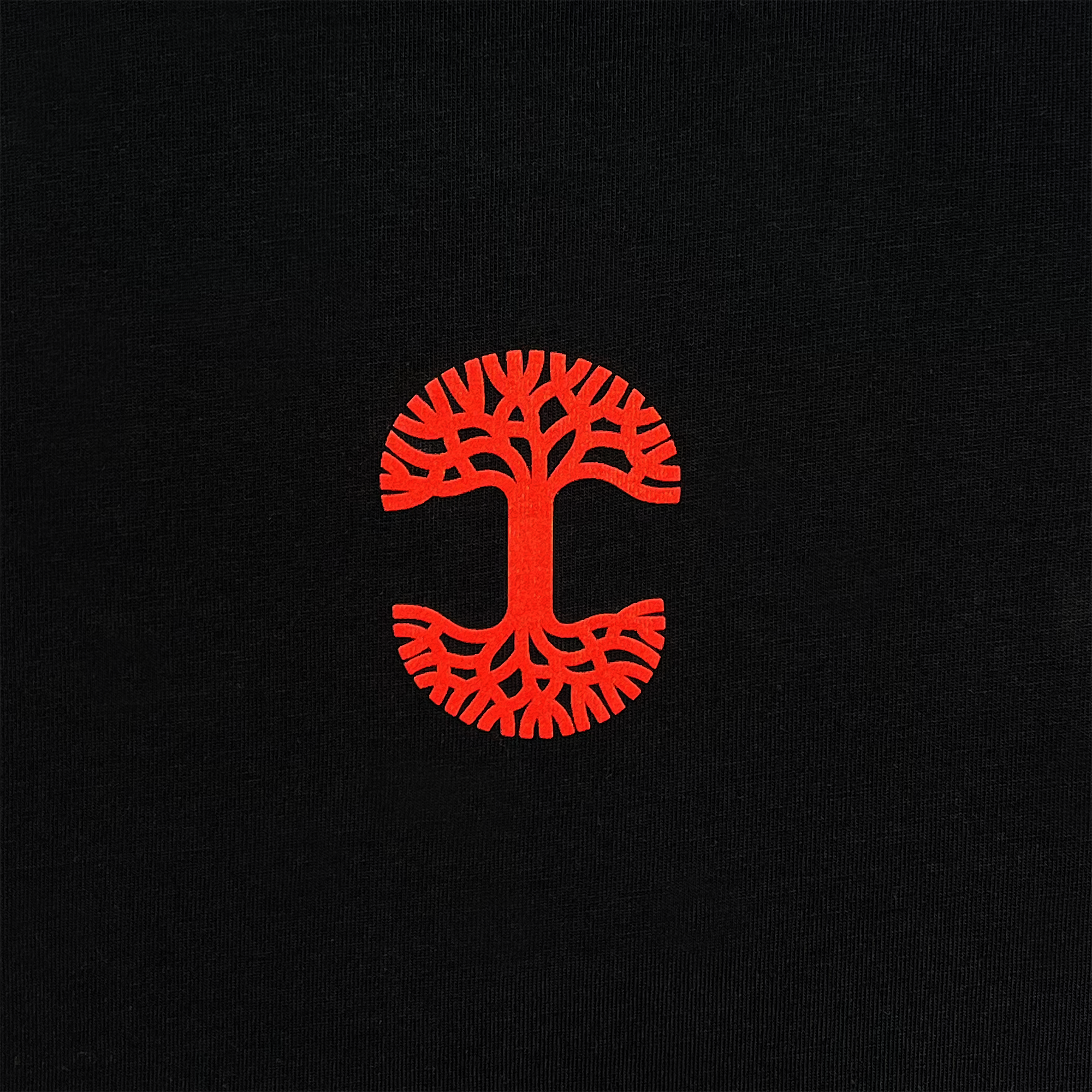 Centered on a black background, the stylized red tree logo symbolizes the Oaklandish brand's collaboration on the "You Got To KYHU LS Tee." The circular design features roots and branches mirroring each other to create a symmetrical pattern, with its simplicity and bold color contrast highlighting Oakland’s cultural significance.