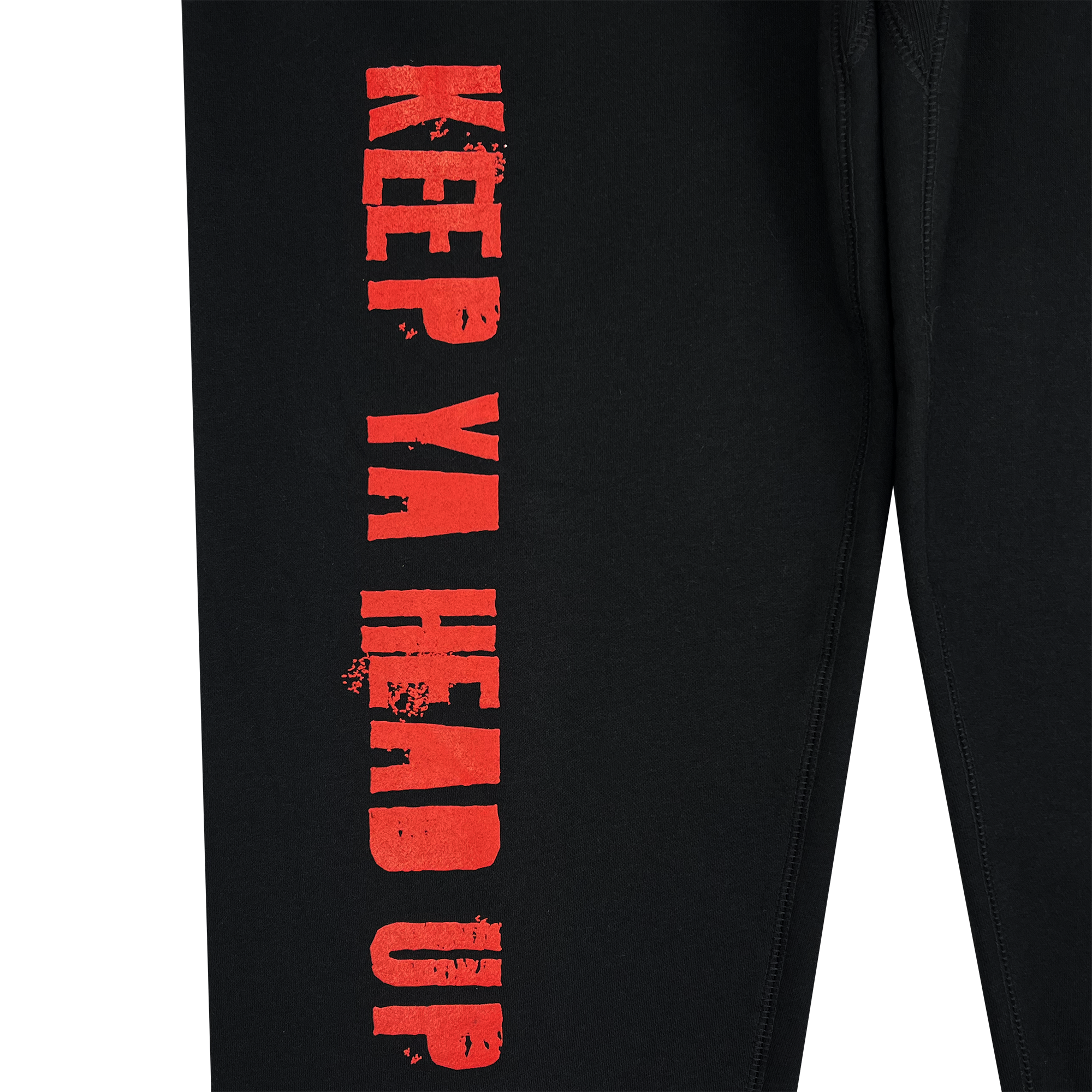 This close-up of black fabric features the phrase "KEEP YA HEAD UP" in bold, distressed red capital letters. It runs parallel to a seam, reminiscent of joggers, and exudes a hip-hop collection vibe. The stitching echoes Oaklandish style, hinting at a Tupac collaboration with the You Got To KYHU Jogger from Oaklandish.