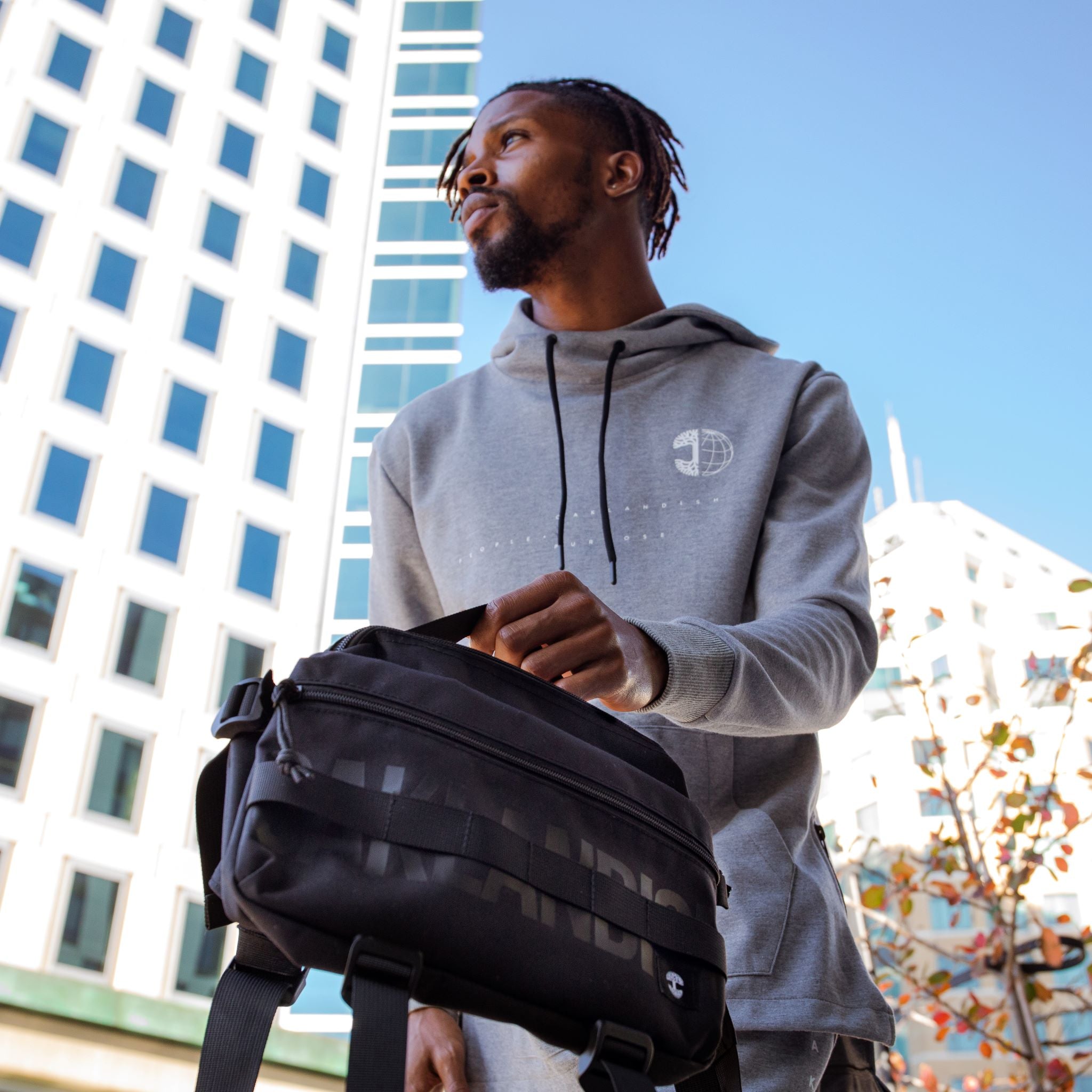 Man on Oakland street in grey Oaklandish jogger set carrying a black nylon hip bag with a black Oaklandish wordmark. 