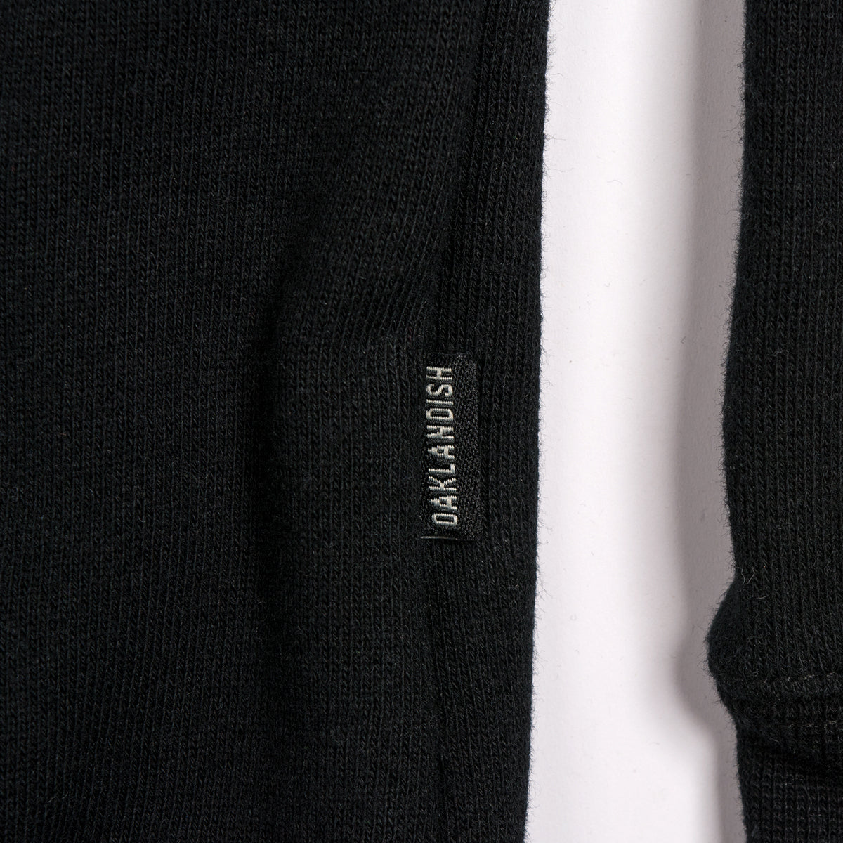 Close-up of a black fabric with a small rectangular label stitched onto it. The label is black with white text that reads "DANIEL AND ASH." The fabric appears to be soft, possibly wool or cotton, and the label is placed near a side seam, reminiscent of the quality you’d find in products like the Oakland Roots SC Logo Crew by Oakland Roots SC.