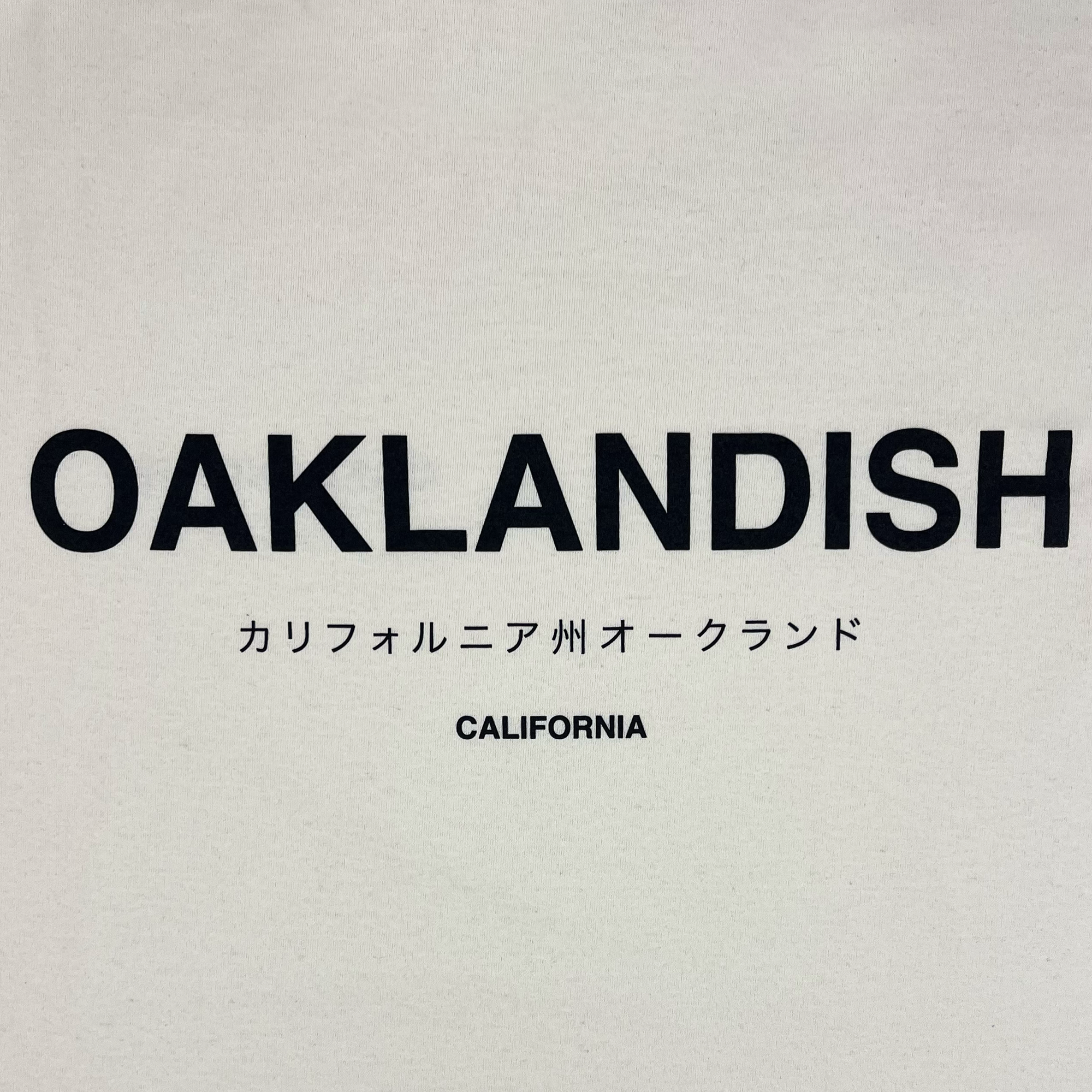 The Modern Type Tee by Oaklandish features a white background with the word "OAKLANDISH" in bold, black uppercase letters. Below, there is Japanese text translating to "California Oakland," and underneath, the word "CALIFORNIA" is written in smaller black uppercase letters. This design graces a classic fit t-shirt from our men's collection, crafted from 100% cotton.