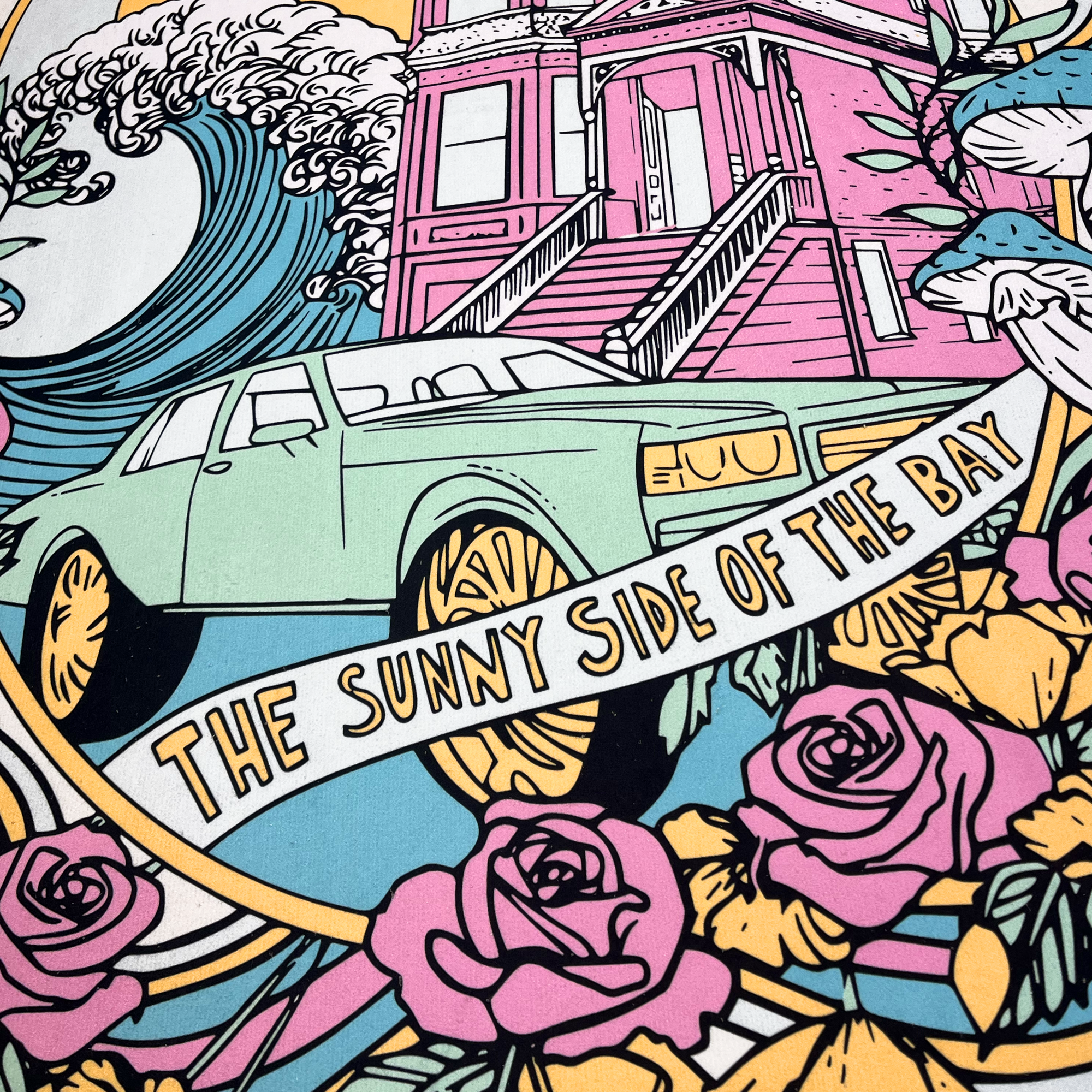 An eye-catching illustration on the Oakland Dream Towel by Oaklandish showcases a mint green car parked in front of a classic San Francisco-style house. The scene is enhanced by surrounding elements like waves, roses, and mushrooms. A bold banner across the image declares "The Sunny Side of the Bay." This Beachside dreamy artwork utilizes bright and pastel colors to create its vibrant aesthetic.