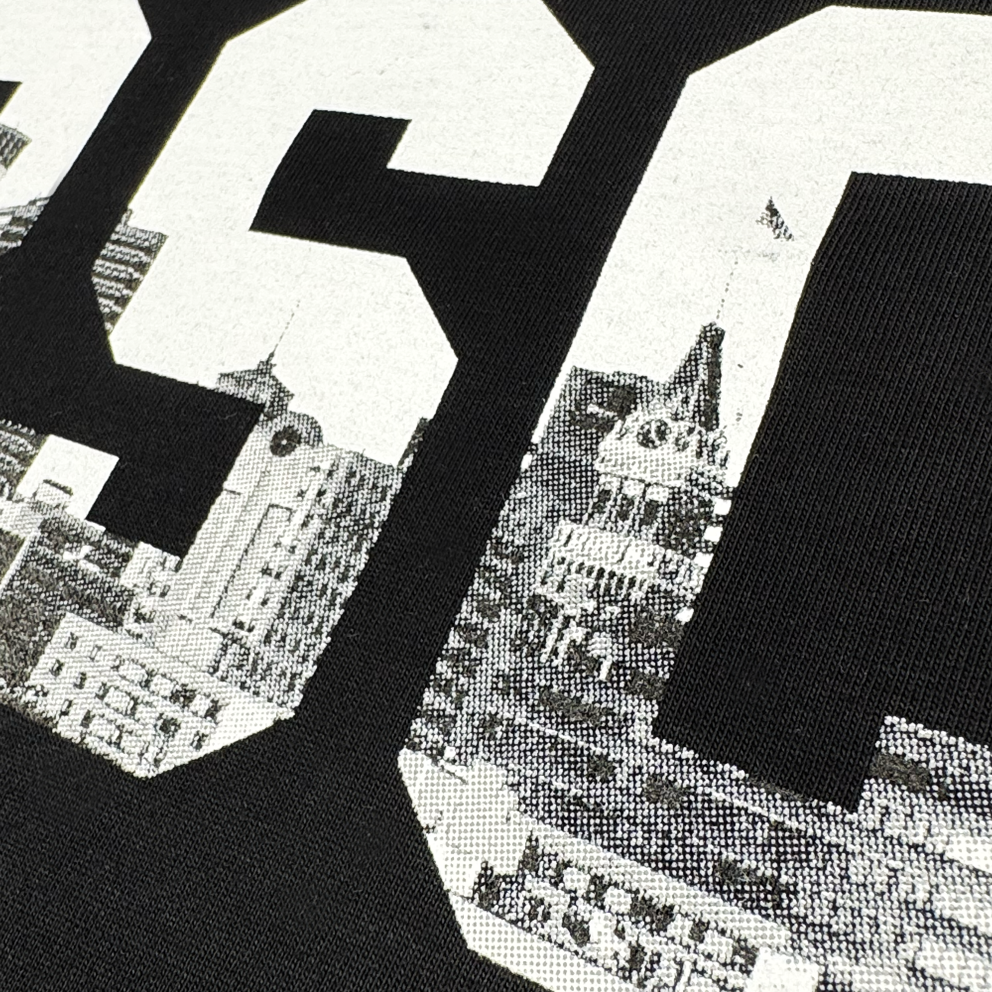 The ORSCtone Tee by Oakland Roots SC showcases large block letters "S C" with intricate architectural details of buildings and a clock tower on a dark background. The design embodies the Oaklandish Classic style, enhancing the sense of social good through its detailed urban art.