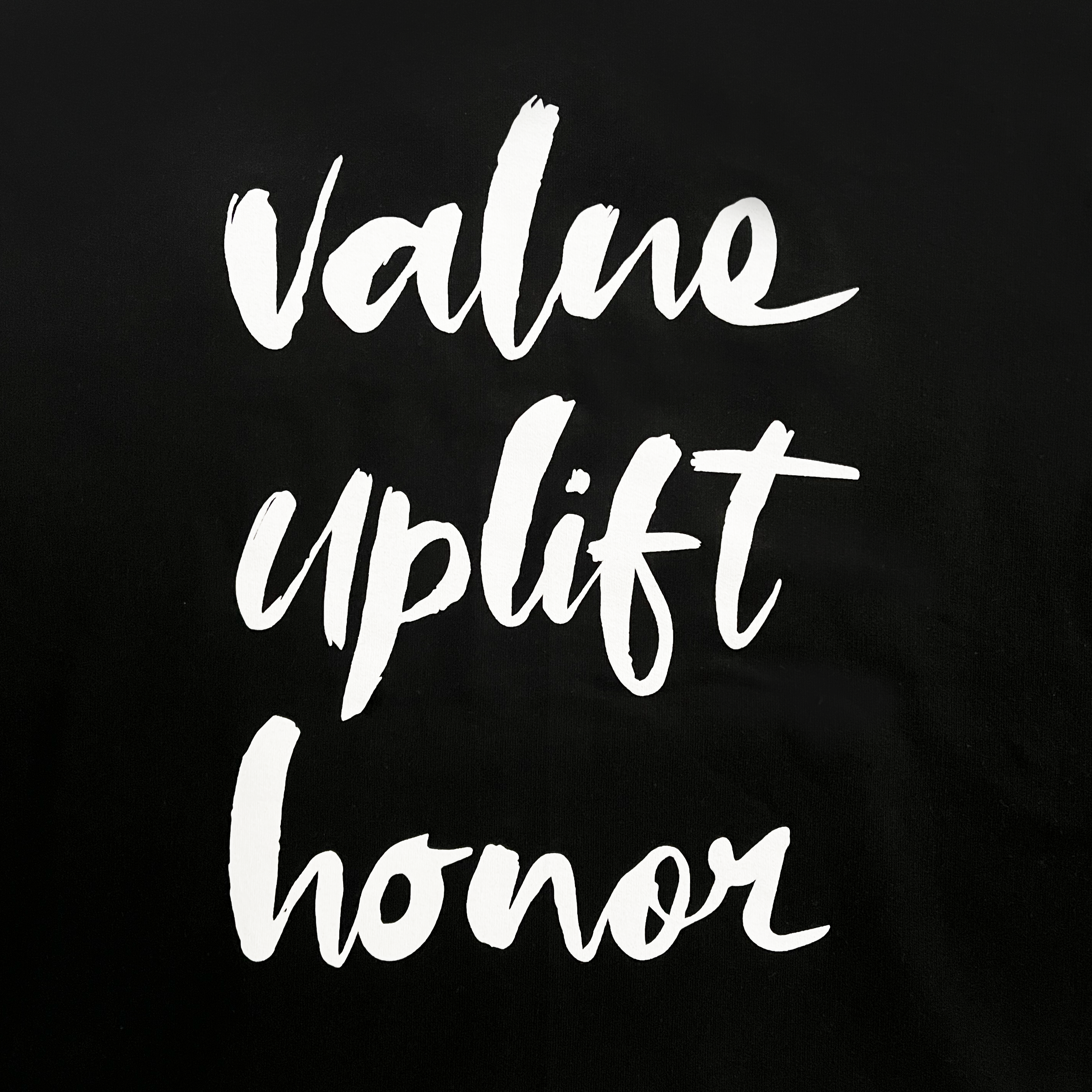 White brushstroke-style text on a solid black background reads "value uplift honor," with each word stacked vertically and centered. The casual, handwritten font gives a bold and uplifting appeal. This design is showcased on the OSA Signature Tee by Supported Brands, capturing the spirit of the Oakland School for the Arts.