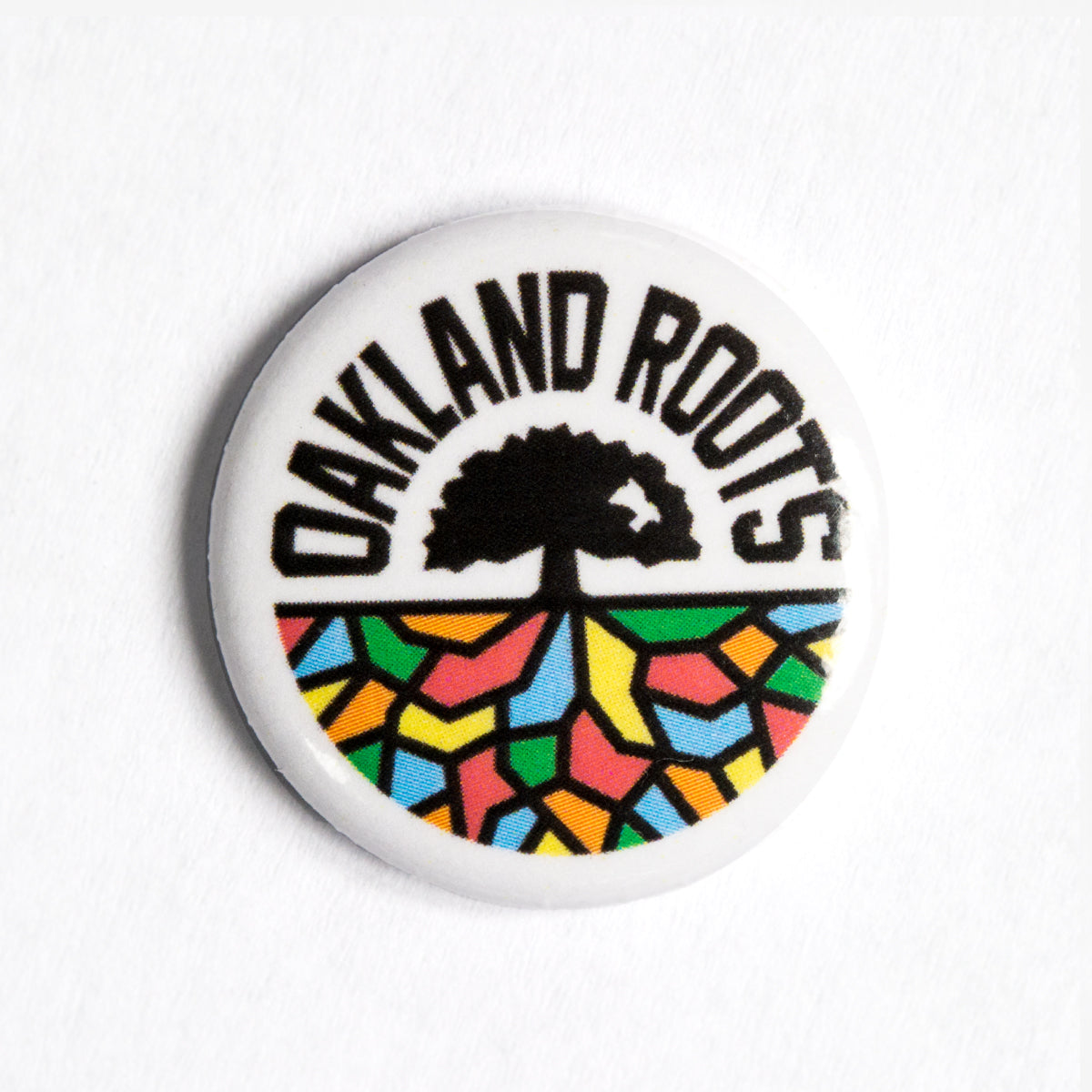 The Oakland Roots SC Pin by Oakland Roots SC features the bold black text "OAKLAND ROOTS" at the top, representing the Oakland Roots Sports Club. Below, a stylized tree outline is set against a vibrant background of colorful mosaic patterns in yellow, red, green, and blue hues.