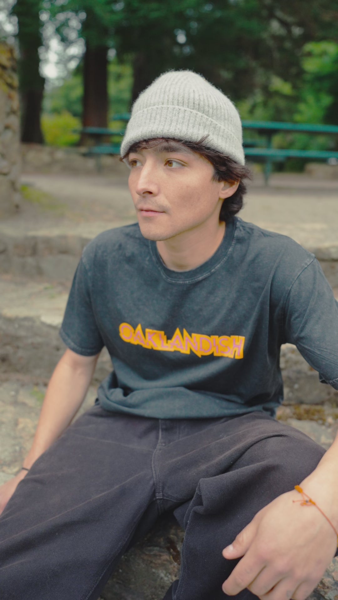 Guy model sitting on some steps outside, wering the Mothership tee, with a beanie on.