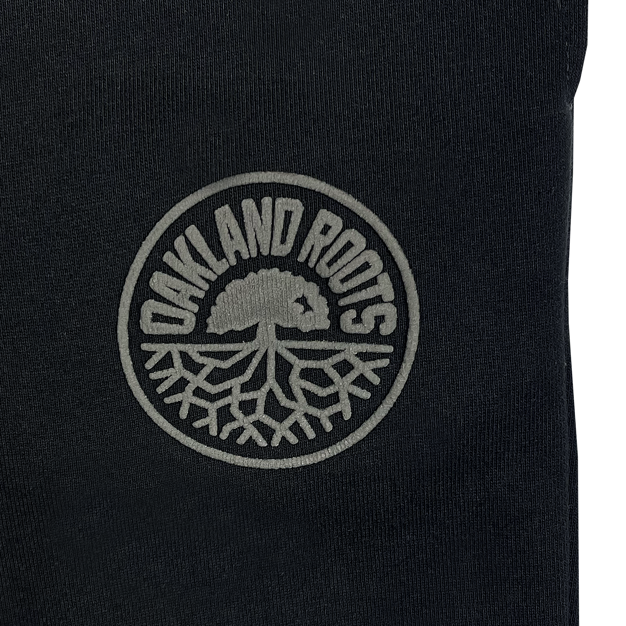 Detailed view of black cotton sweatpants with tonal imprint Oakland Roots SC crest near left pocket.