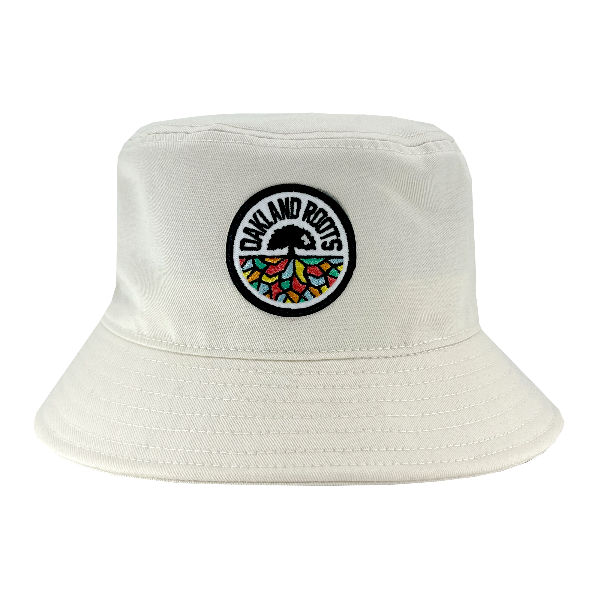 The Oakland Roots SC Bucket Hat, by Oakland Roots SC, showcases a light-colored design with an embroidered circular patch on the front. The patch features a tree with colorful segments and roots, encircled by the text "Oakland Roots," celebrating the local sports club. The hat also includes detailed stitching along the brim and crown.