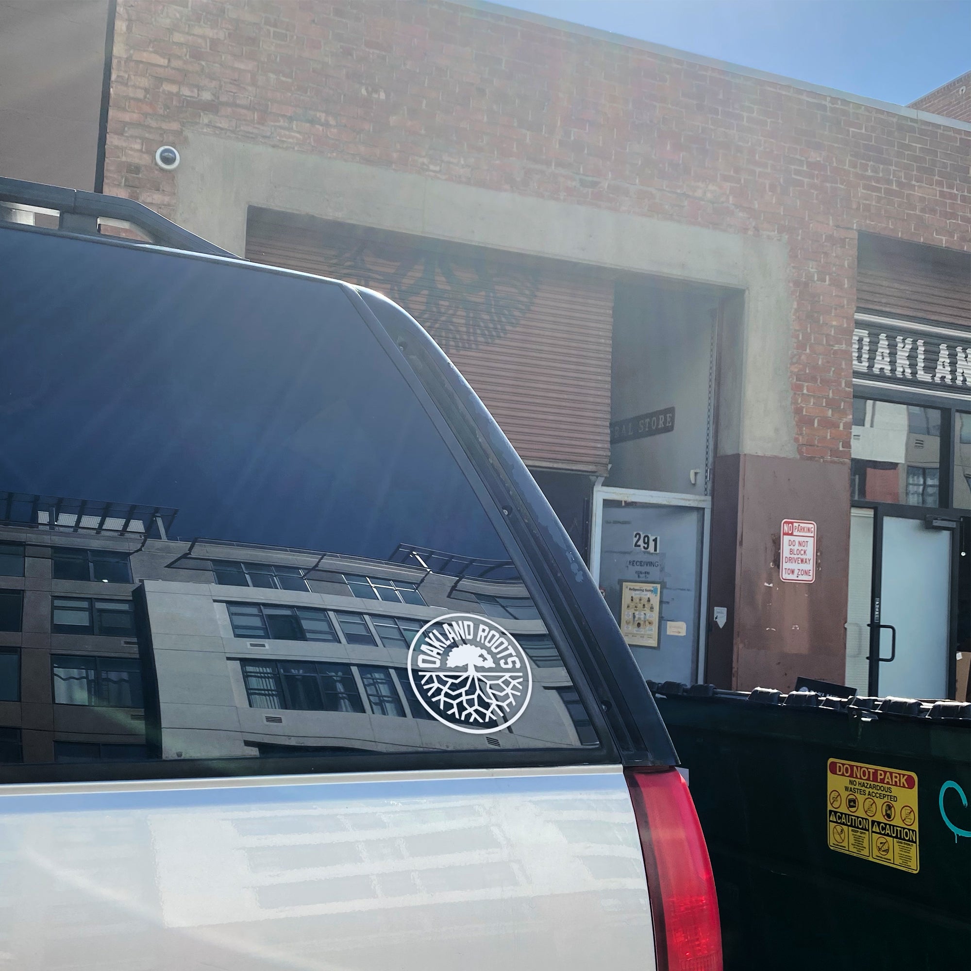 White circular Oakland Roots logo on a 6” in diameter car window decal sticker on the back window of a white SUV.