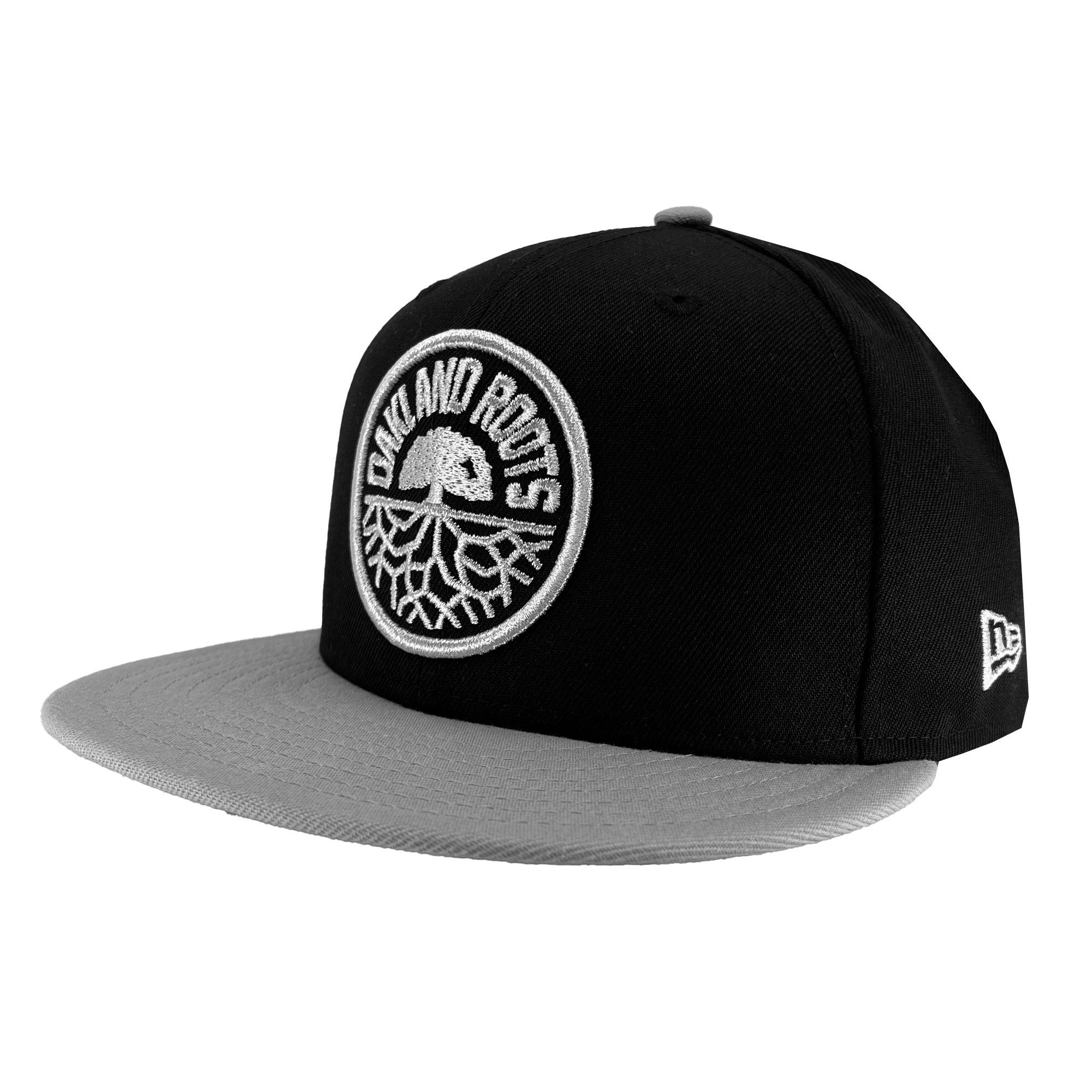 The New Era Oakland Roots SC 59FIFTY Cap by Oakland Roots SC features a black body with a gray brim and displays a circular patch on the front, showcasing a white oak tree with roots and the text "Oakland Roots." The New Era logo is also embroidered on the side of this stylish sports club accessory.