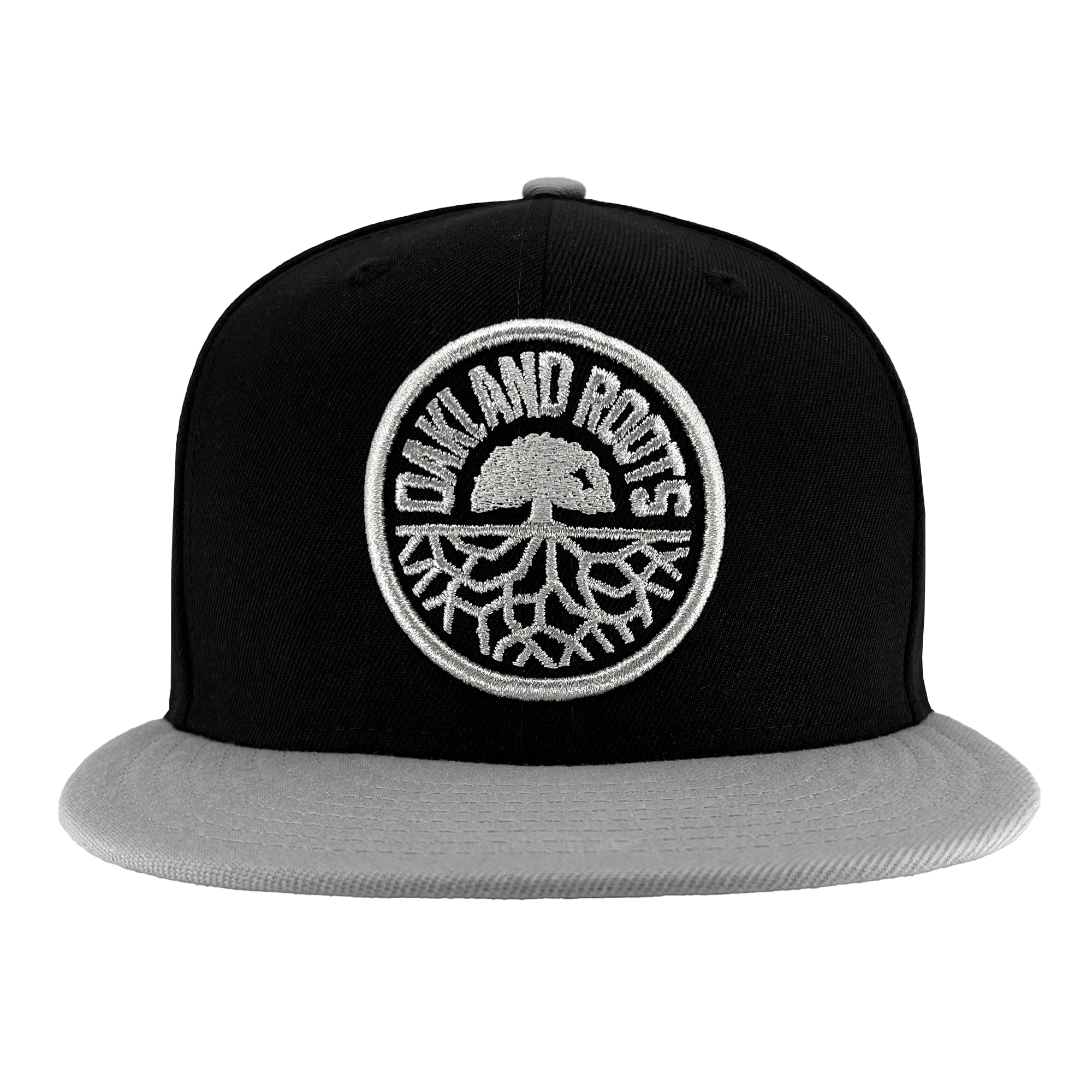 The New Era Oakland Roots SC 59FIFTY Cap, crafted by Oakland Roots SC, features a black cap with a grey brim. It showcases an embroidered white circular logo depicting a tree with roots extending beneath it. The text "OAKLAND ROOTS," representative of the sports club, is arranged in a semicircle around the top of the tree within the circle.