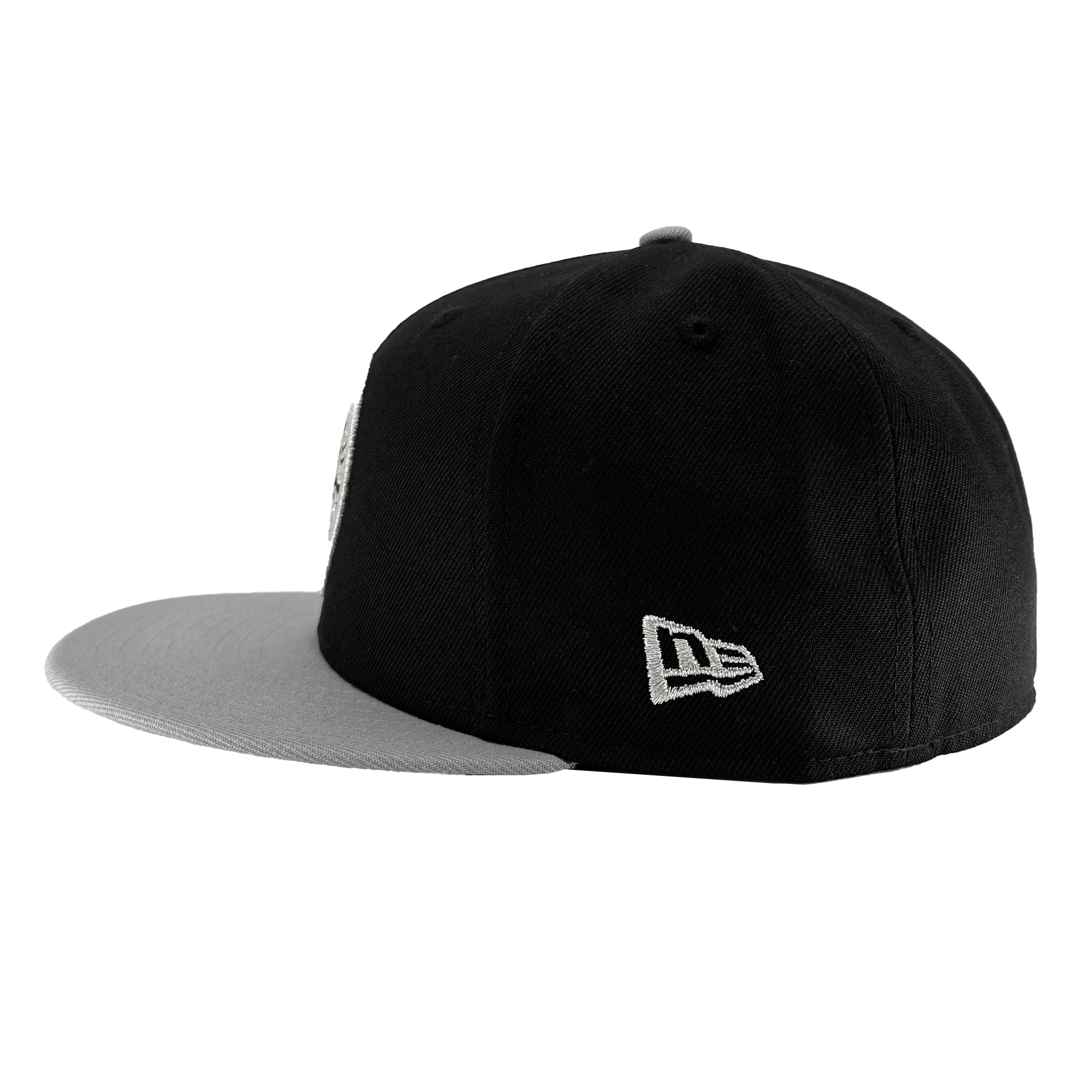 Introducing the New Era Oakland Roots SC 59FIFTY Cap by Oakland Roots SC. This stylish cap features a bold black color with an eye-catching flat gray brim. Adorning the cap is a small white Oakland Roots logo on the left side near the brim, complemented by another white emblem on the right side. The cap's two-tone color scheme and detailed embroidery are showcased from a side angle, making it a perfect accessory for any sports club fan.