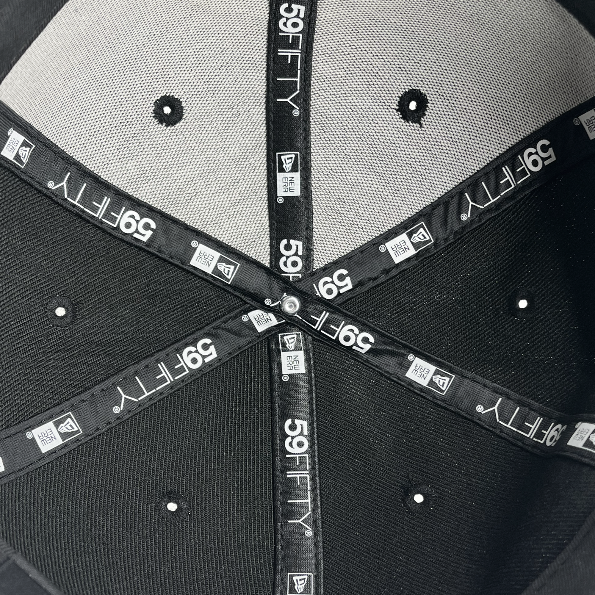 Inside view of a New Era Oakland Roots SC 59FIFTY fitted cap. The picture showcases the hat's interior, highlighting the black seams and labels with "59FIFTY" printed in white multiple times along the inner lining. The top of the cap features a grey fabric panel. Six small ventilation holes are also visible, making it perfect for any Oakland Roots SC fan.