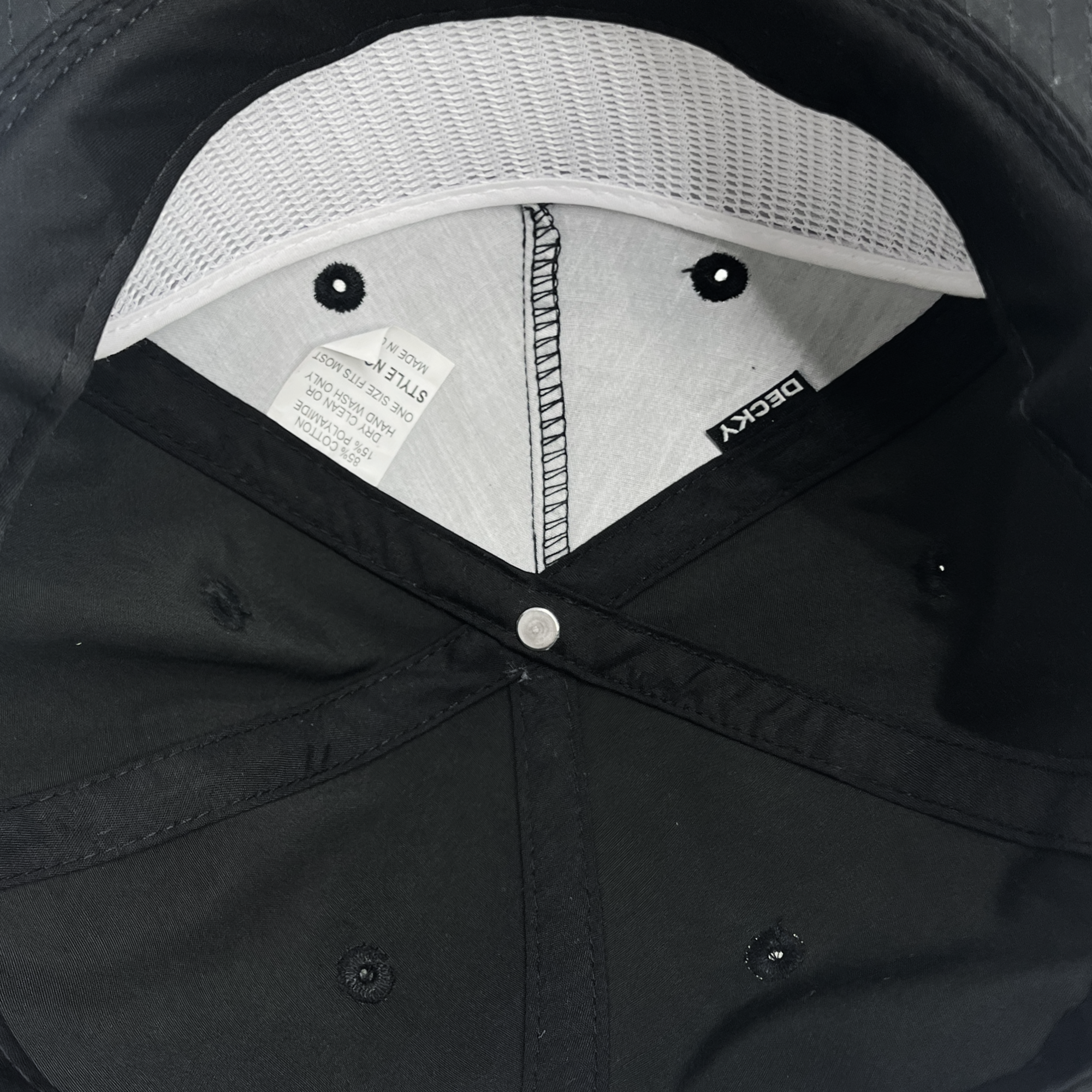 Inside view of the Heritage Cap displaying the inner lining and brand labels. The label offers care instructions and identifies the brand as "Oakland Roots SC." Ideal for your next visit to an Oakland Roots game, this cap features a grey mesh inner lining for breathability, a black button at the top center, and black fabric panels with eyelets for ventilation.