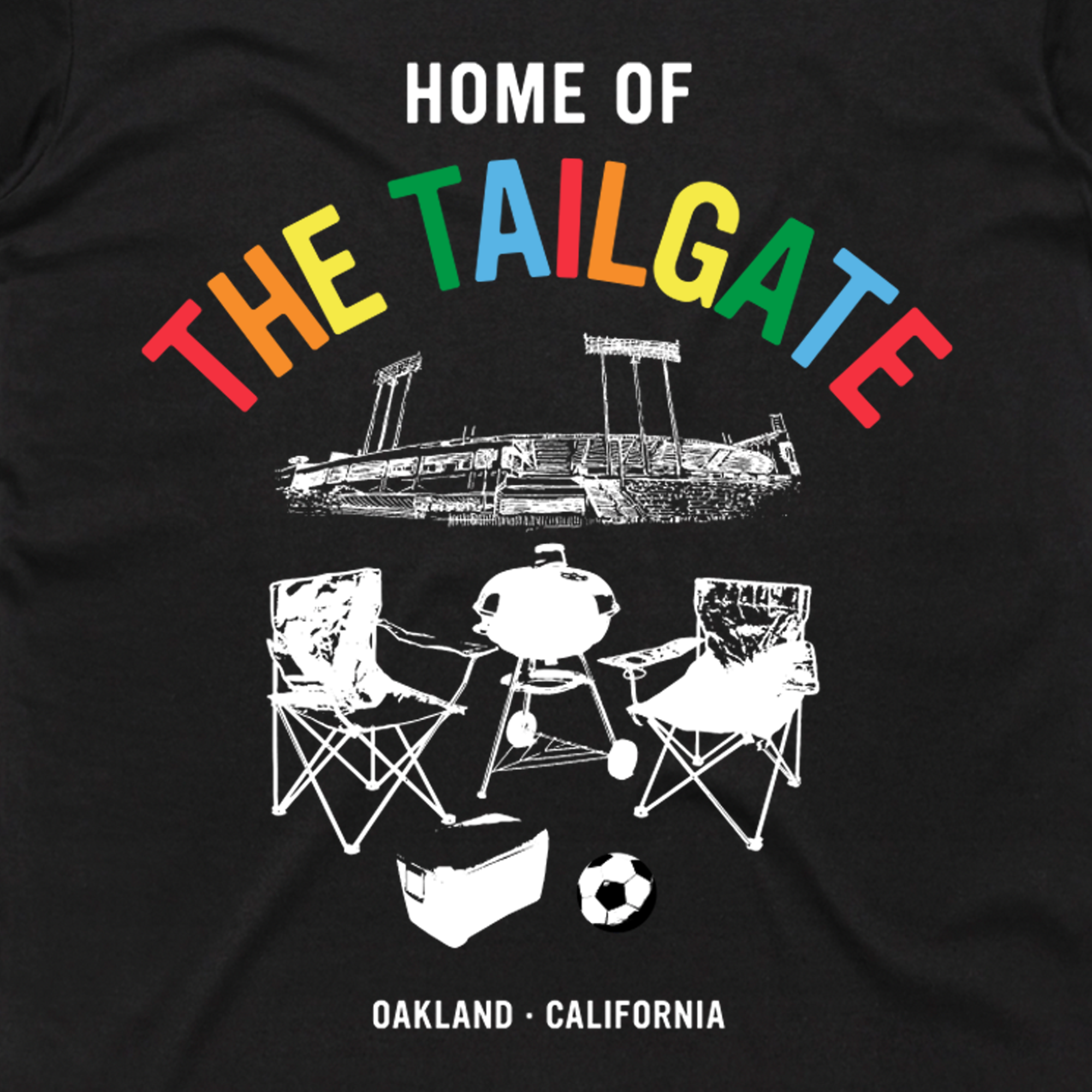 The "Home of the Tailgate Tee" from Oaklandish’s Men's collection showcases bold, colorful lettering above a white stadium silhouette. A sketch of folding chairs, a grill, cooler, and soccer ball adds charm below, with "Oakland - California" at the bottom. Made from 100% cotton for a classic fit.