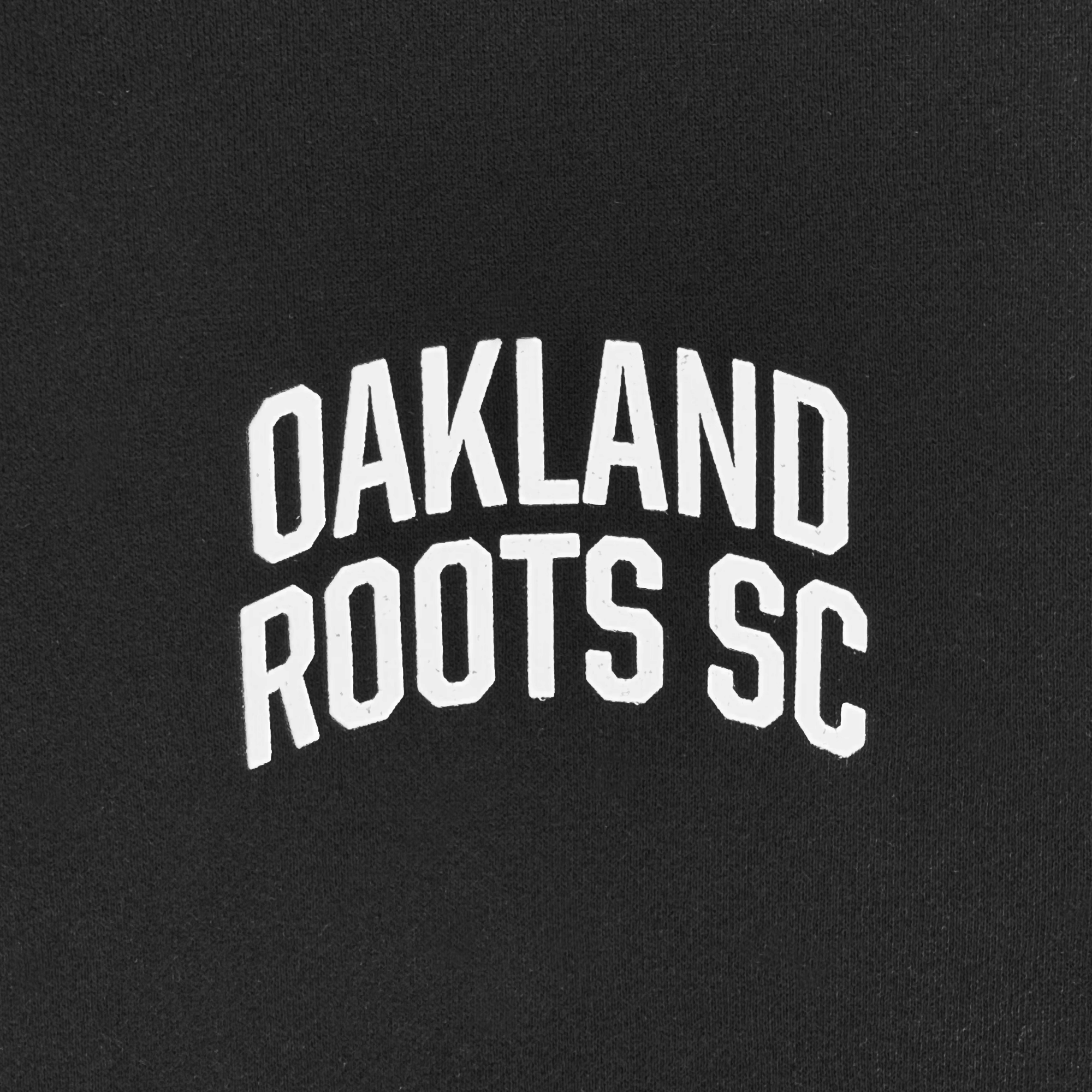 Black hoodie with a bold, white, arched "OAKLAND ROOTS SC" text, representing a sports club dedicated to social good.