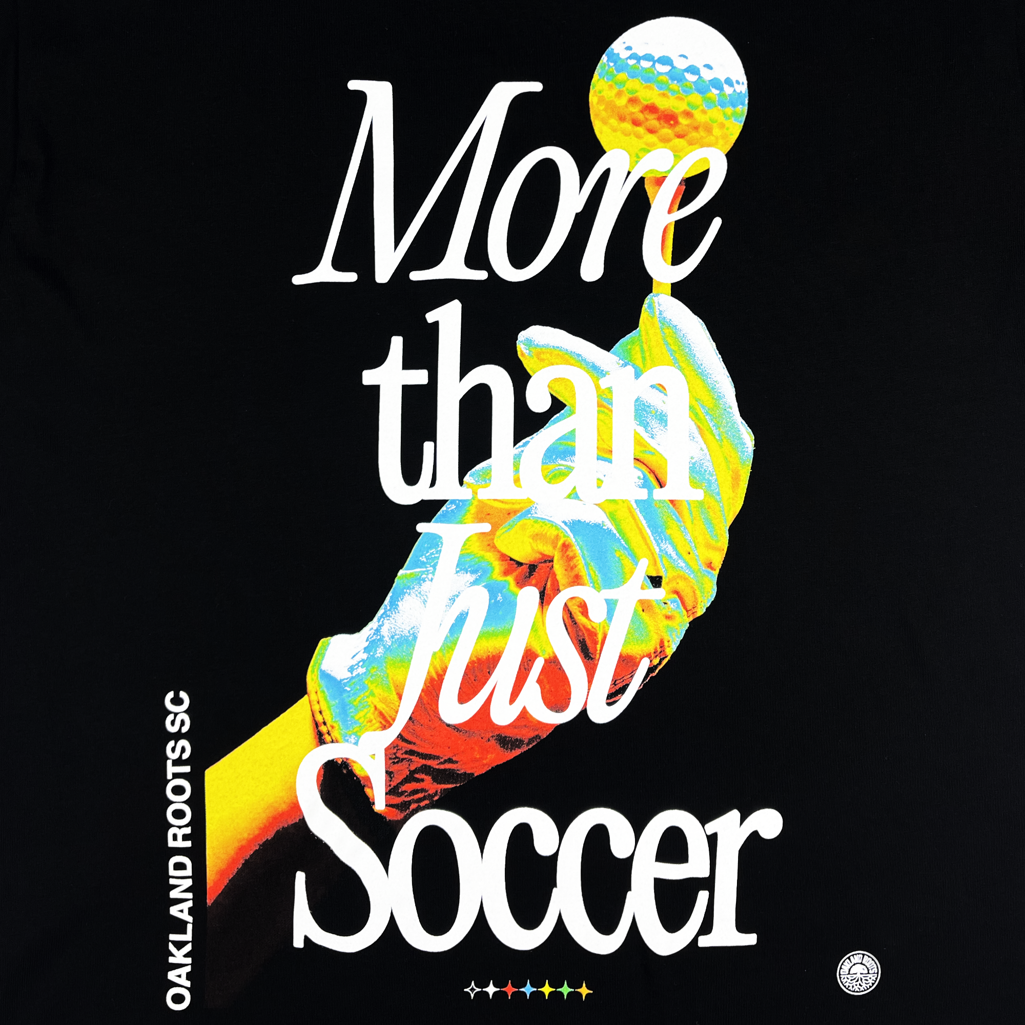 The More Than Soccer Tee features a black background with a brightly colored, stylized hand holding a globe-like soccer ball. Large white text over the hand reads "More than just Soccer." Below this text, in smaller print, are the words "Oakland Roots SC" and a small circular logo. A five-star sequence in rainbow colors is displayed beneath the main text.