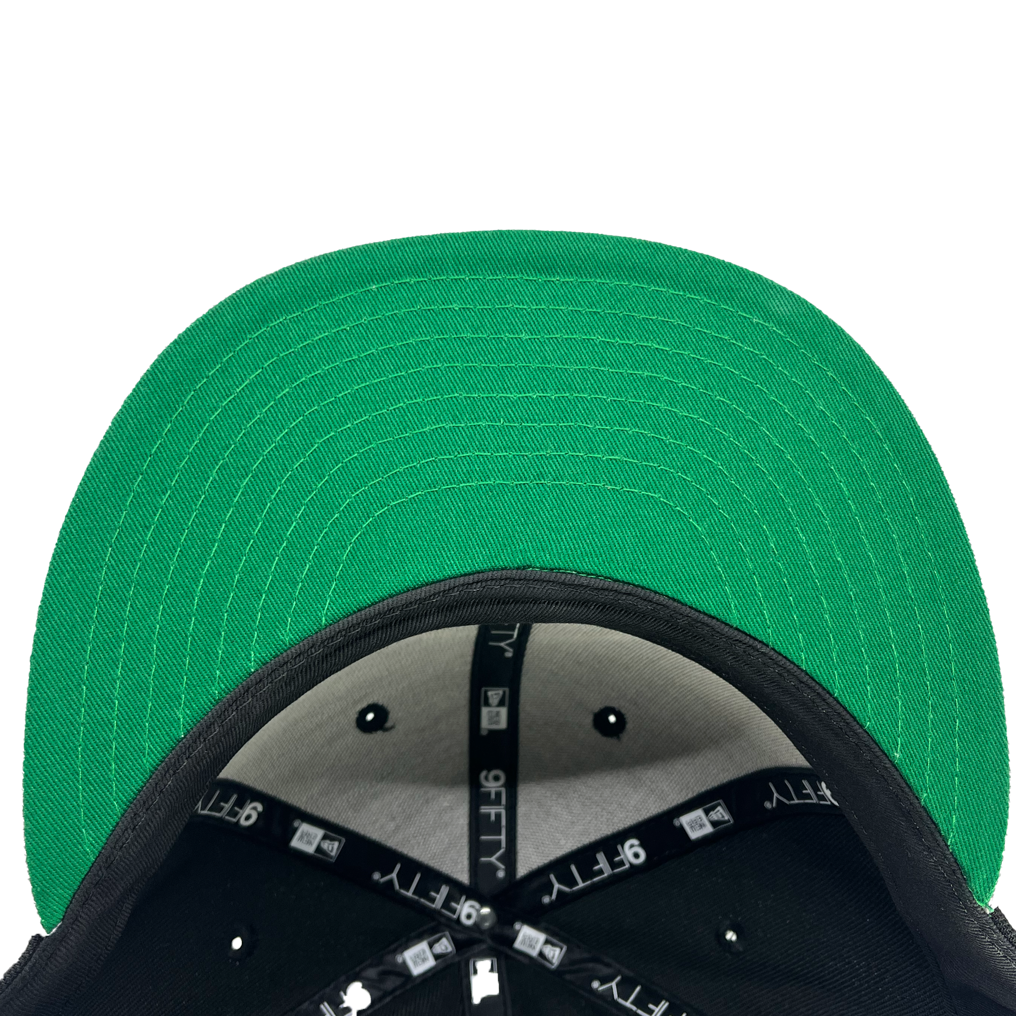 A top-down view of the New Era Oakland Roots SC 9FIFTY cap reveals a black exterior paired with a green underbrim. The underside showcases visible black lining with "9FIFTY" branding in white, complemented by black and white stitching across the panels. The inner part displays connectors and stitching details, emphasizing its structured design, making it perfect for any Oakland Roots SC fan.