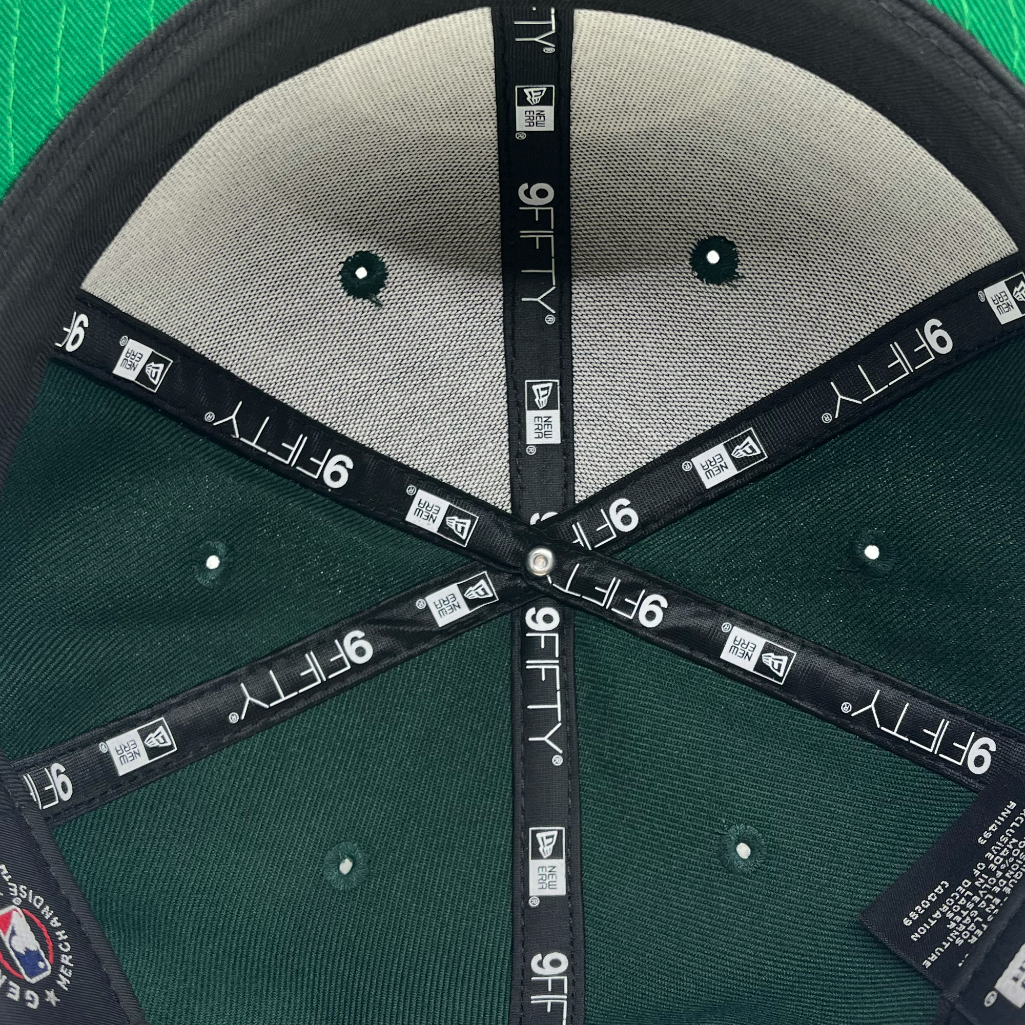 The interior of the New Era Oakland Roots SC 9FIFTY Cap is shown. The cap's panels are held together by black tape with white "9FIFTY" text printed repeatedly. The green fabric on the underside contrasts with the grey inner panels. A tag with the Oakland Roots SC brand logo and care instructions is visible along the seam, reflecting its pride in the Oakland Roots sports club.