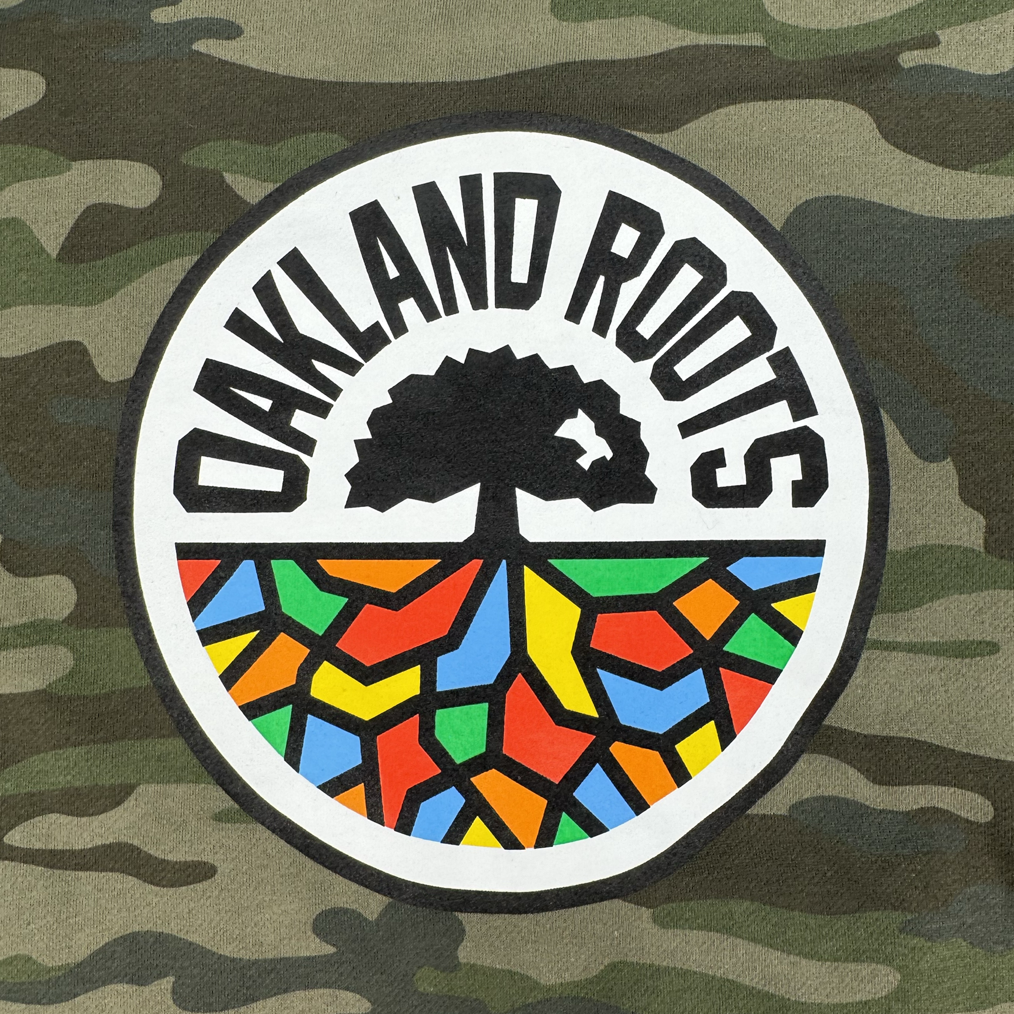 The Oakland Roots SC Classic Zip Hoodie by Oakland Roots SC features a stylized tree silhouette with "OAKLAND ROOTS" above it. Below, vibrant abstract shapes in red, yellow, blue, and orange fill the semicircle like roots, representing the club's colorful heritage.