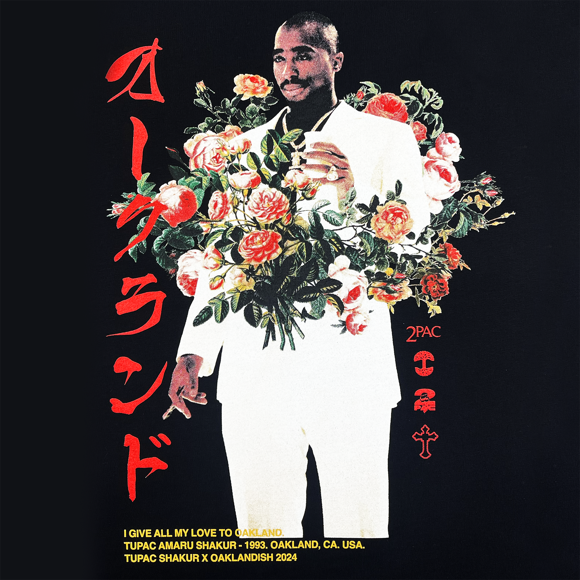 A man in a white suit holds a bouquet of vibrant flowers. Red Japanese characters are on the left. Below, text reads: "I GIVE ALL MY LOVE TO OAKLAND - TUPAC AMARU SHAKUR - 1993." This tribute to Tupac's legacy celebrates the Oaklandish Roses Hoodie from the Tupac hip-hop collection, with a cross symbol and "2PAC" visible.