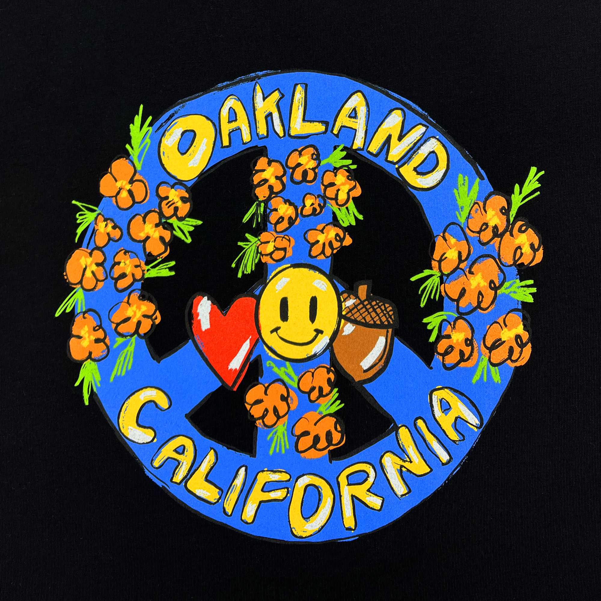 The Smile Tee by Oaklandish showcases a vibrant design with "Oakland California" boldly written in yellow, encircled by a blue peace sign. The text is surrounded by orange floral illustrations, a red heart, a yellow smiley face, and an acorn, all set against a black background. This eye-catching print is perfectly applied on a 100% cotton, classic fit t-shirt.