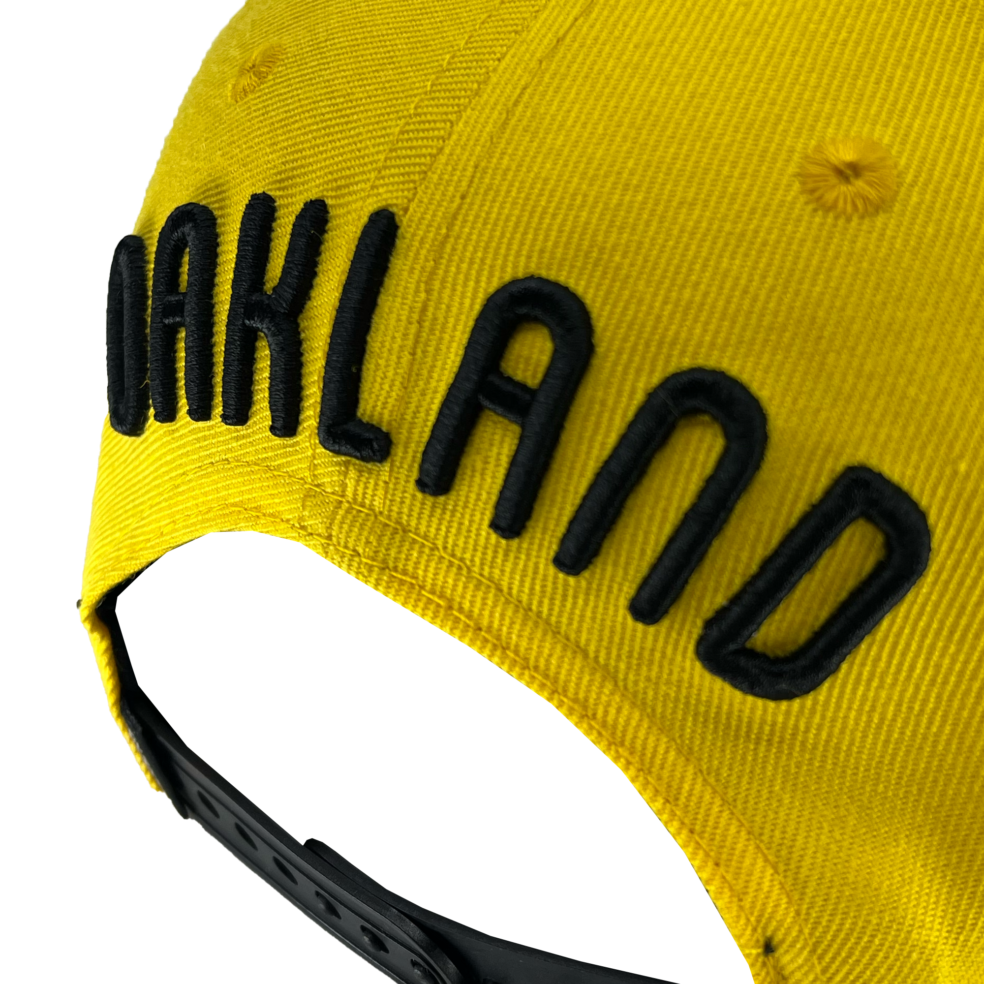 Detailed angle view of yellow snapback hat with 'Oakland' text above arch and oaklandish woven label near black plastic closure.