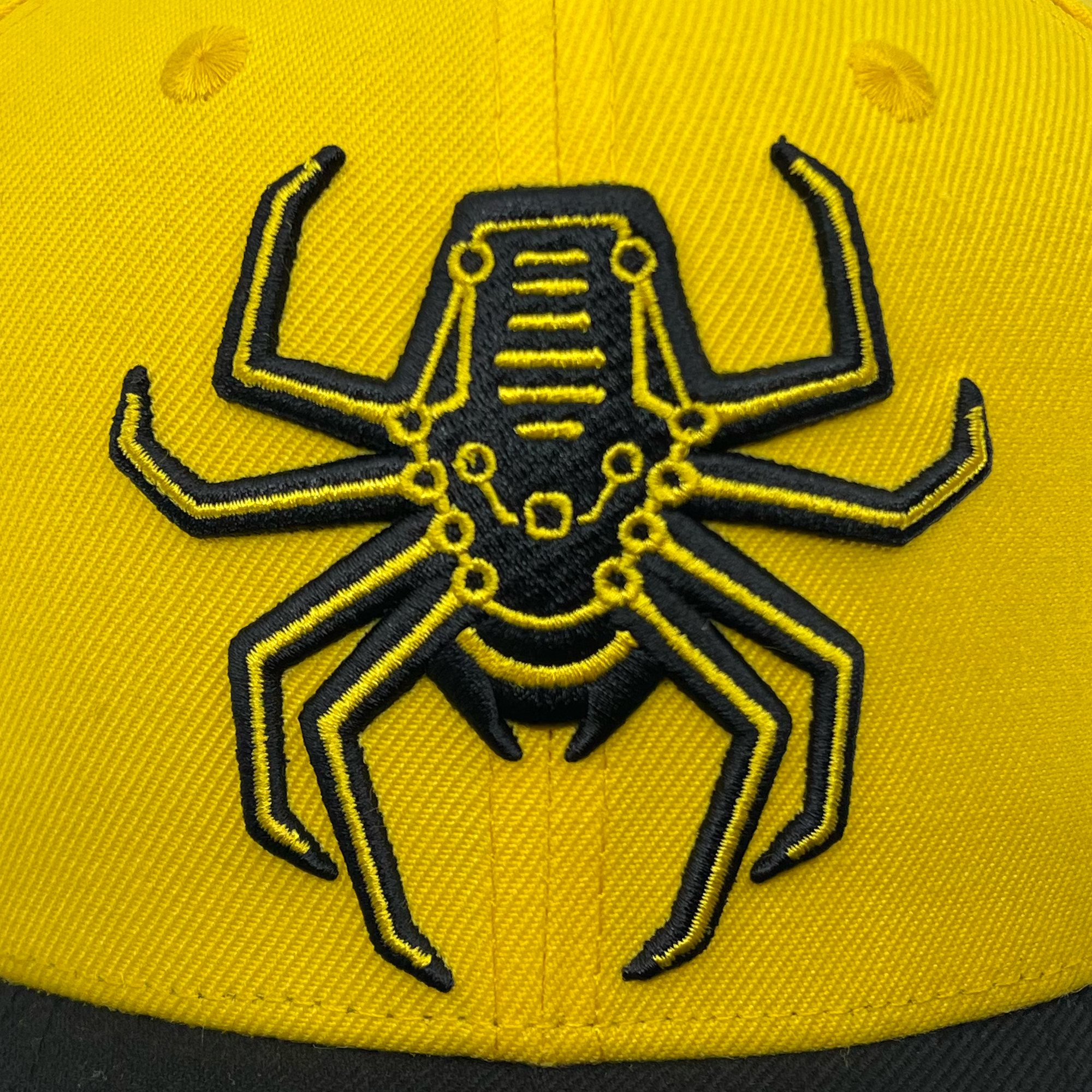 Detailed view of yellow snapback hat with Oakland Spiders logo on crown and black brim.