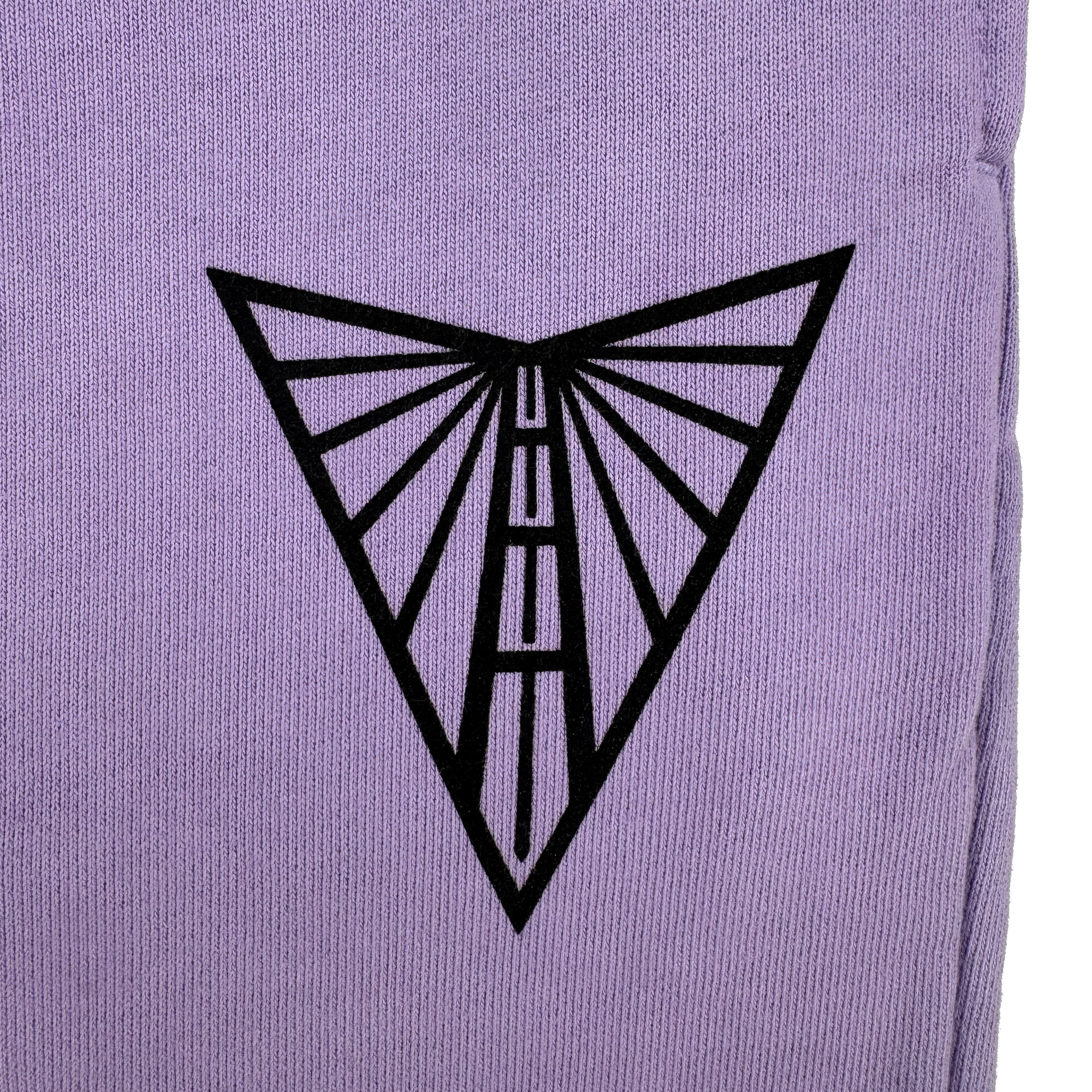 The Golden State Valkyries Primary Heavy Sweatpants by GSV feature a black geometric design on organic cotton. A purple surface displays a downward-pointing triangle, with radiating lines forming an abstract moth or butterfly wing pattern on textured fabric.